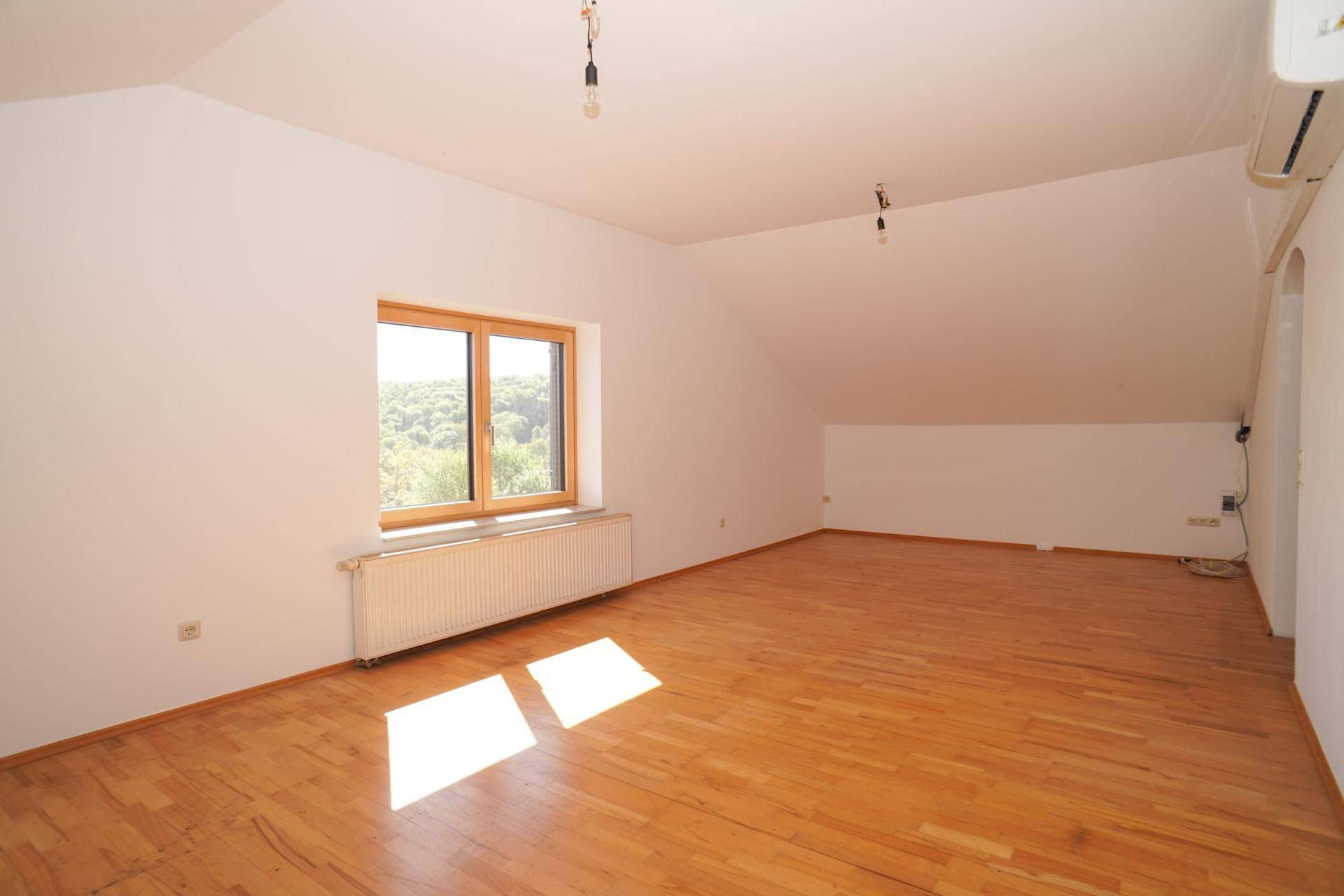 Dachzimmer mit Holzboden, Fenster und Klimaanlage, bietet vielseitige Nutzungsmöglichkeiten.