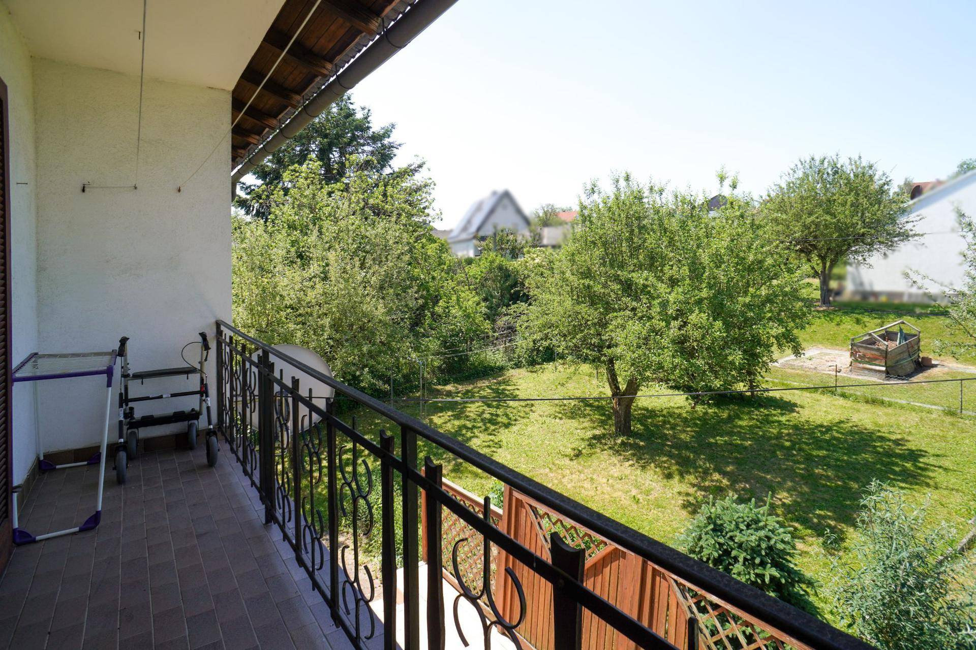 Balkon mit schmiedeeisernem Geländer und weitem Blick über den grünen Garten.
