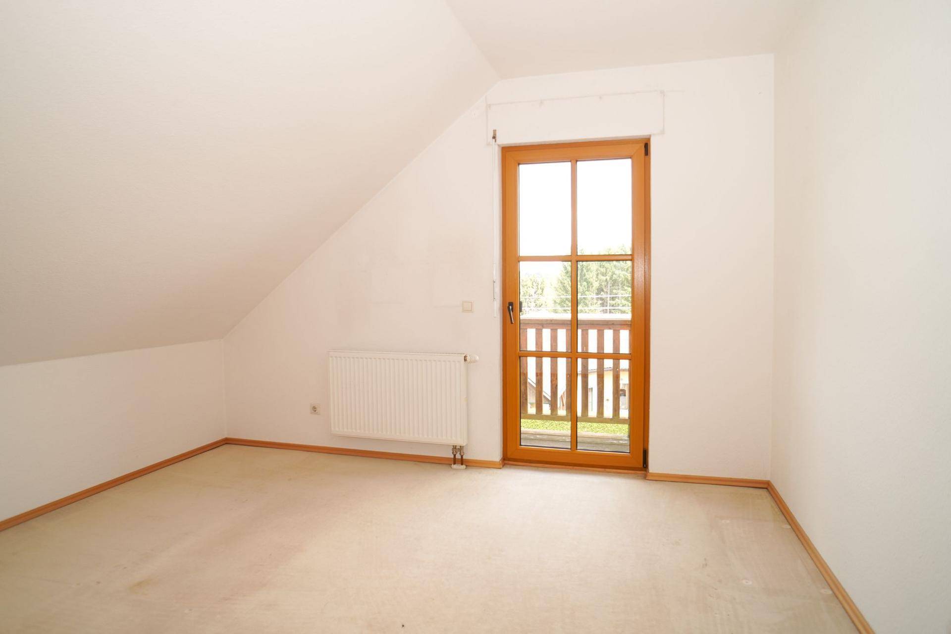 Dachgeschoss-Schlafzimmer mit Teppichboden, Dachschräge und Balkontür, die viel Licht hereinlässt.
