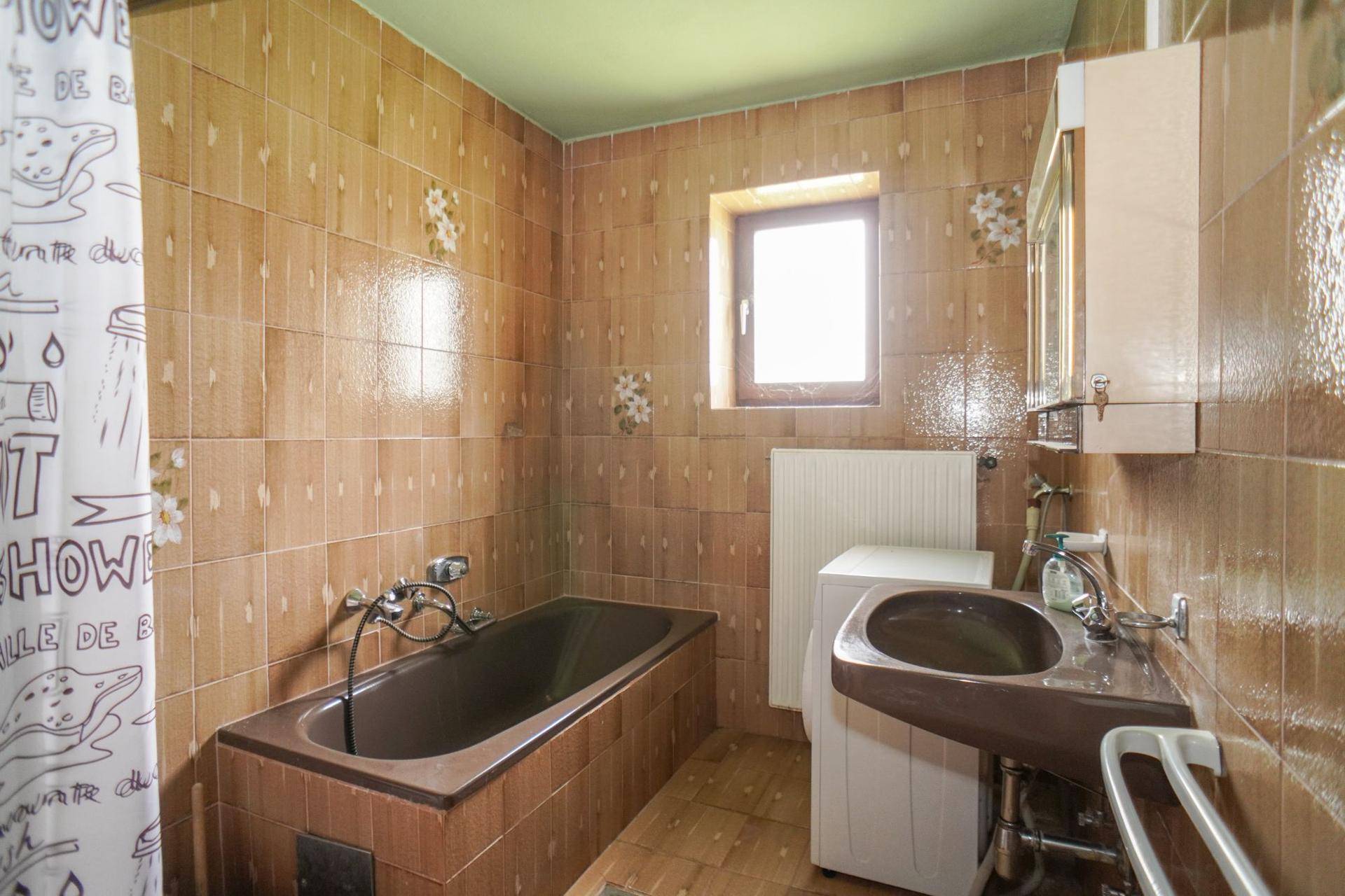 Badezimmer mit braunen Fliesen, Badewanne, Waschbecken und einem kleinen Fenster.
