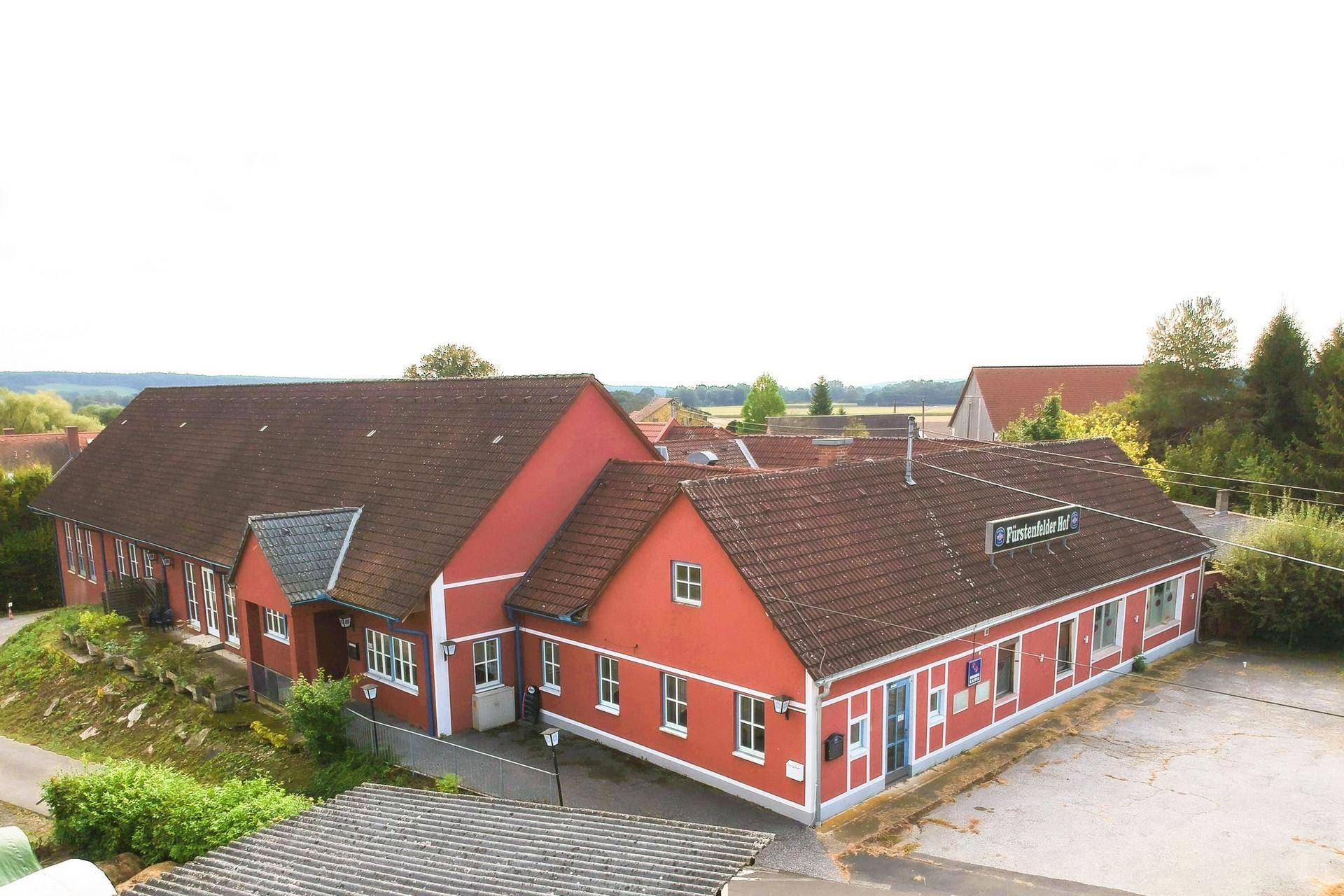 Luftaufnahme des roten Gebäudes mit braunem Ziegeldach und umliegendem Gelände.