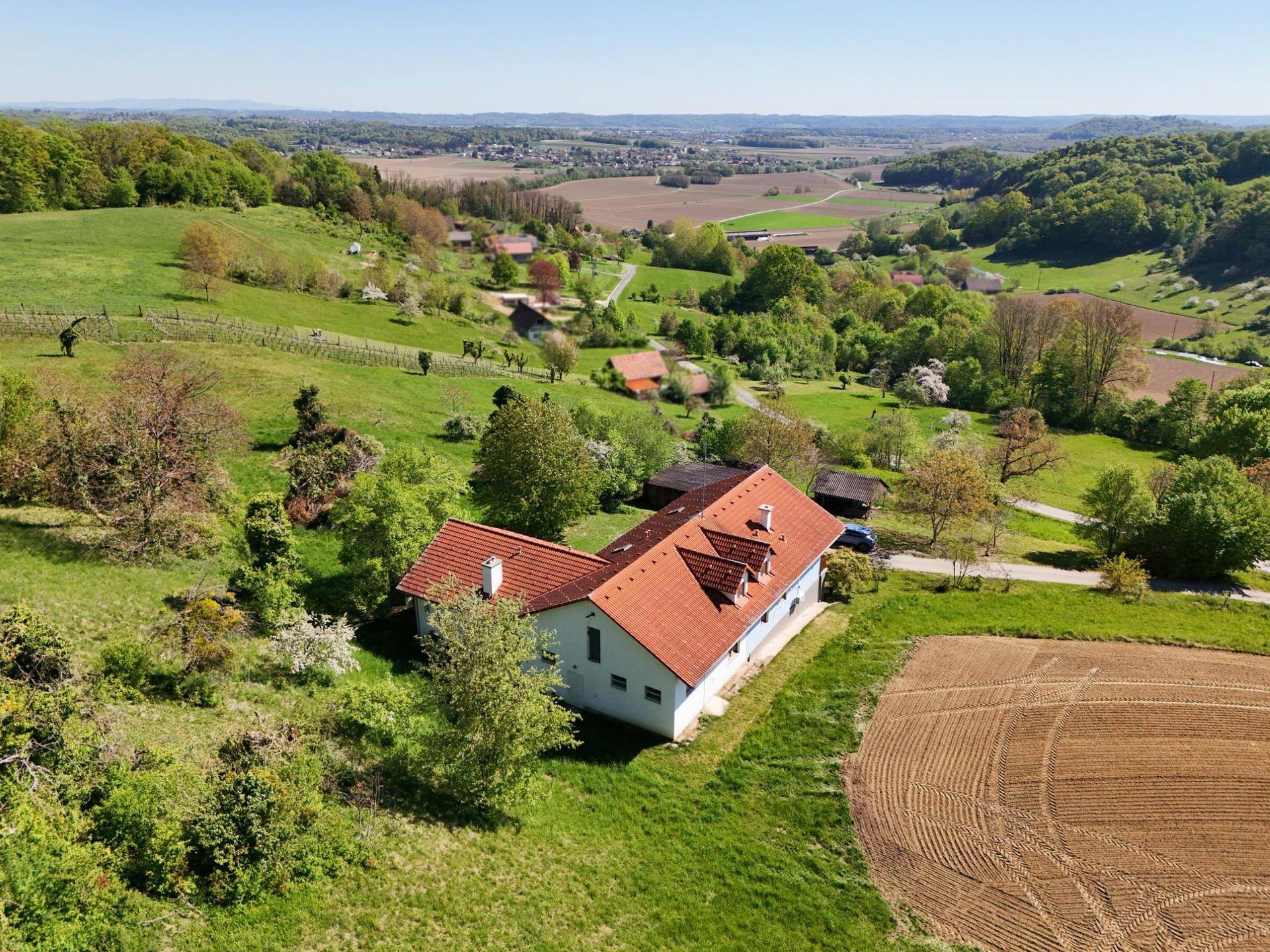 Weitläufige Luftaufnahme eines Hauses in hügeliger Landschaft mit Feldern und Wäldern.