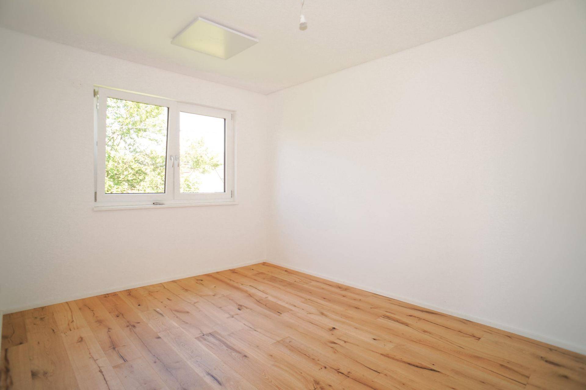 Helles Schlafzimmer mit Holzboden und einem Fenster, das den Blick ins Grüne ermöglicht.