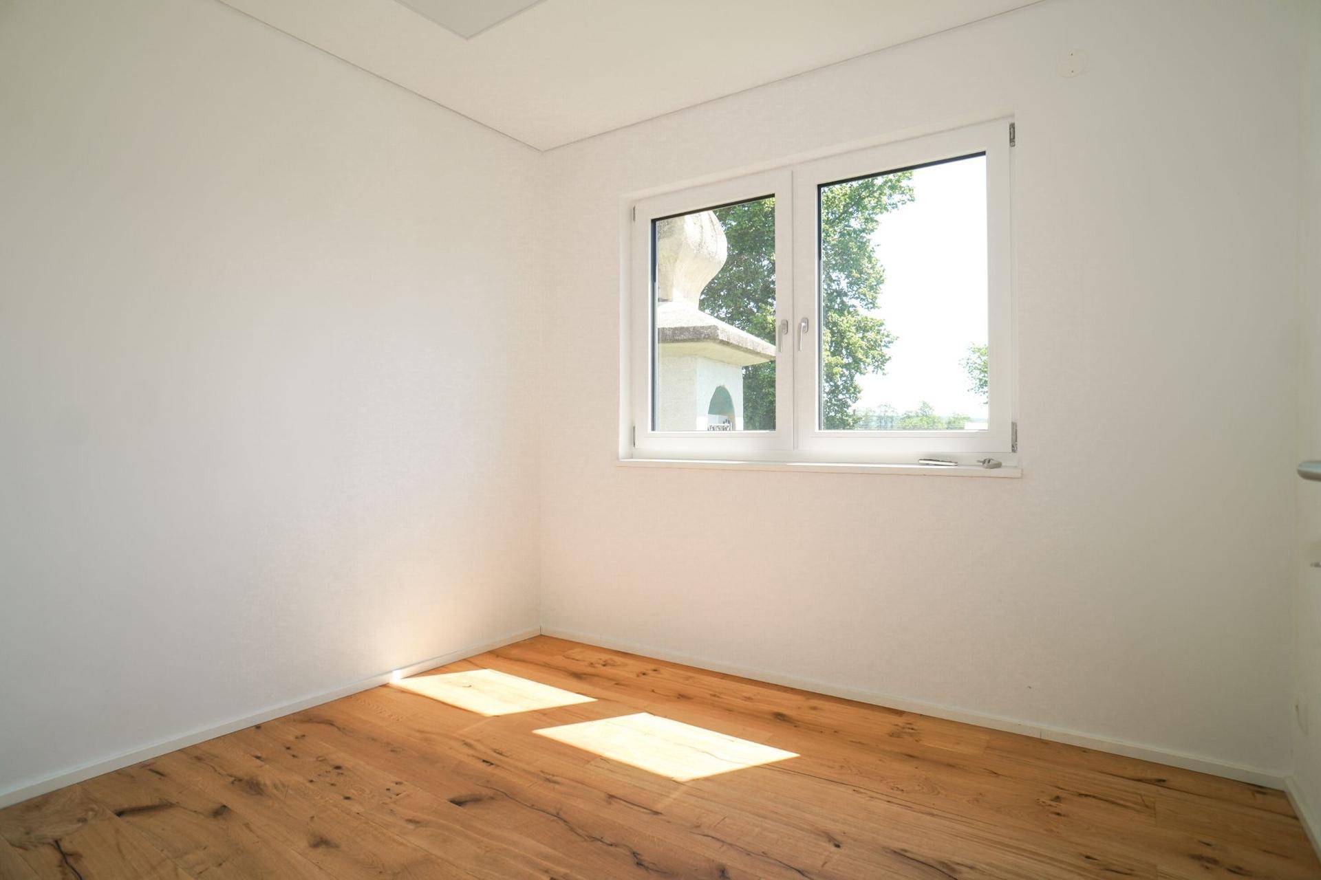 Helles Schlafzimmer mit Holzboden und einem Fenster, das viel Tageslicht hereinlässt.