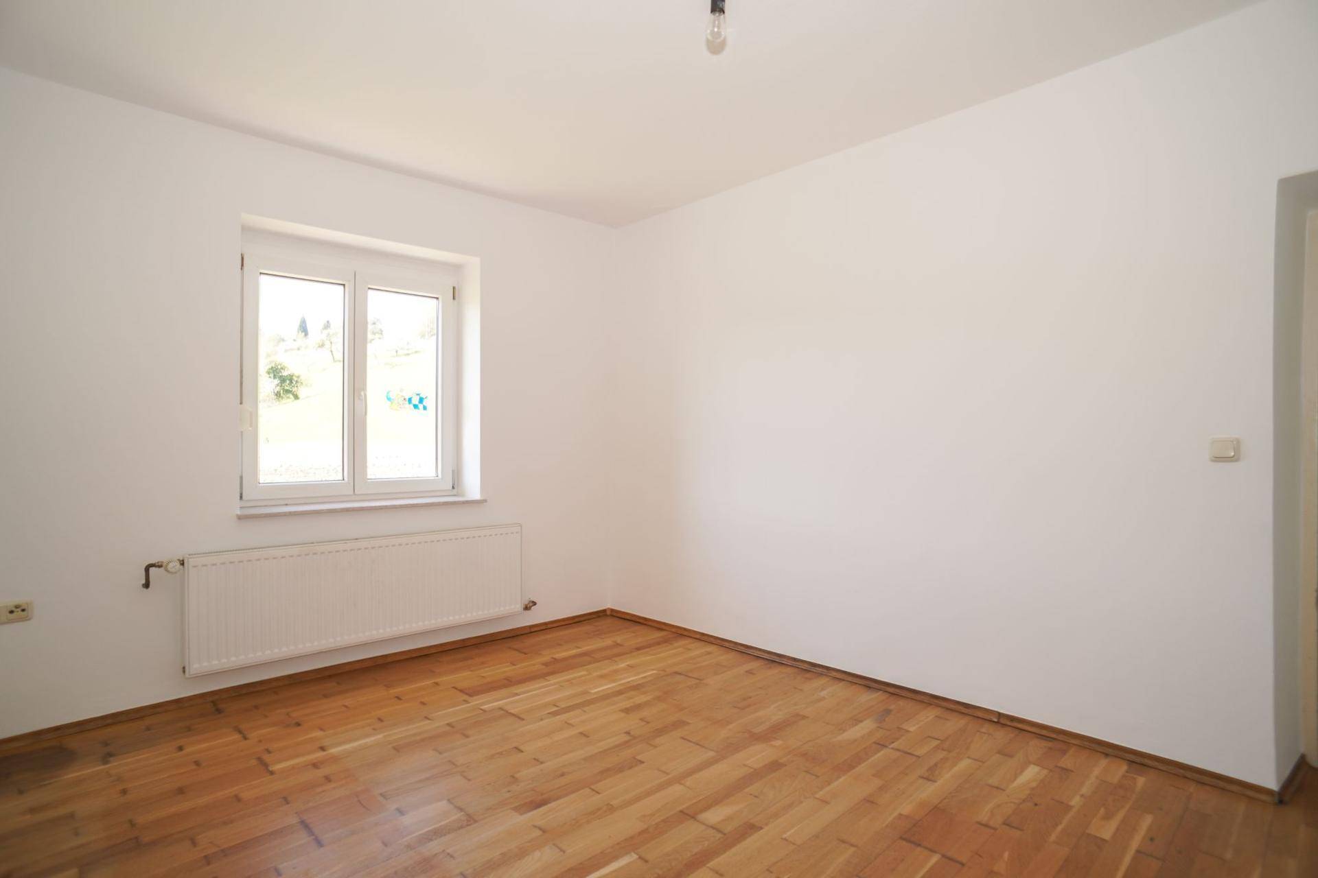Freundliches Zimmer mit Holzboden und Fenster, das viel Tageslicht hereinlässt.
