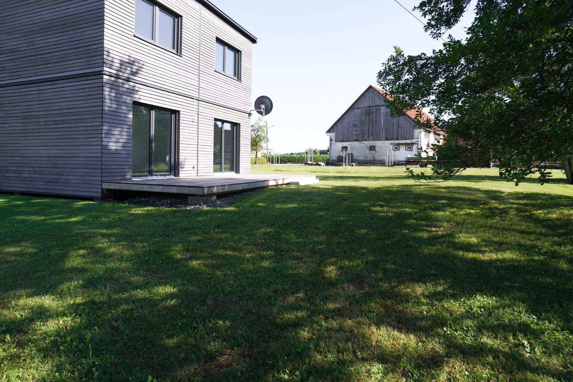 Weitläufiger Gartenbereich neben dem modernen Neubau mit Holzfassade und angrenzender Holzterrasse.