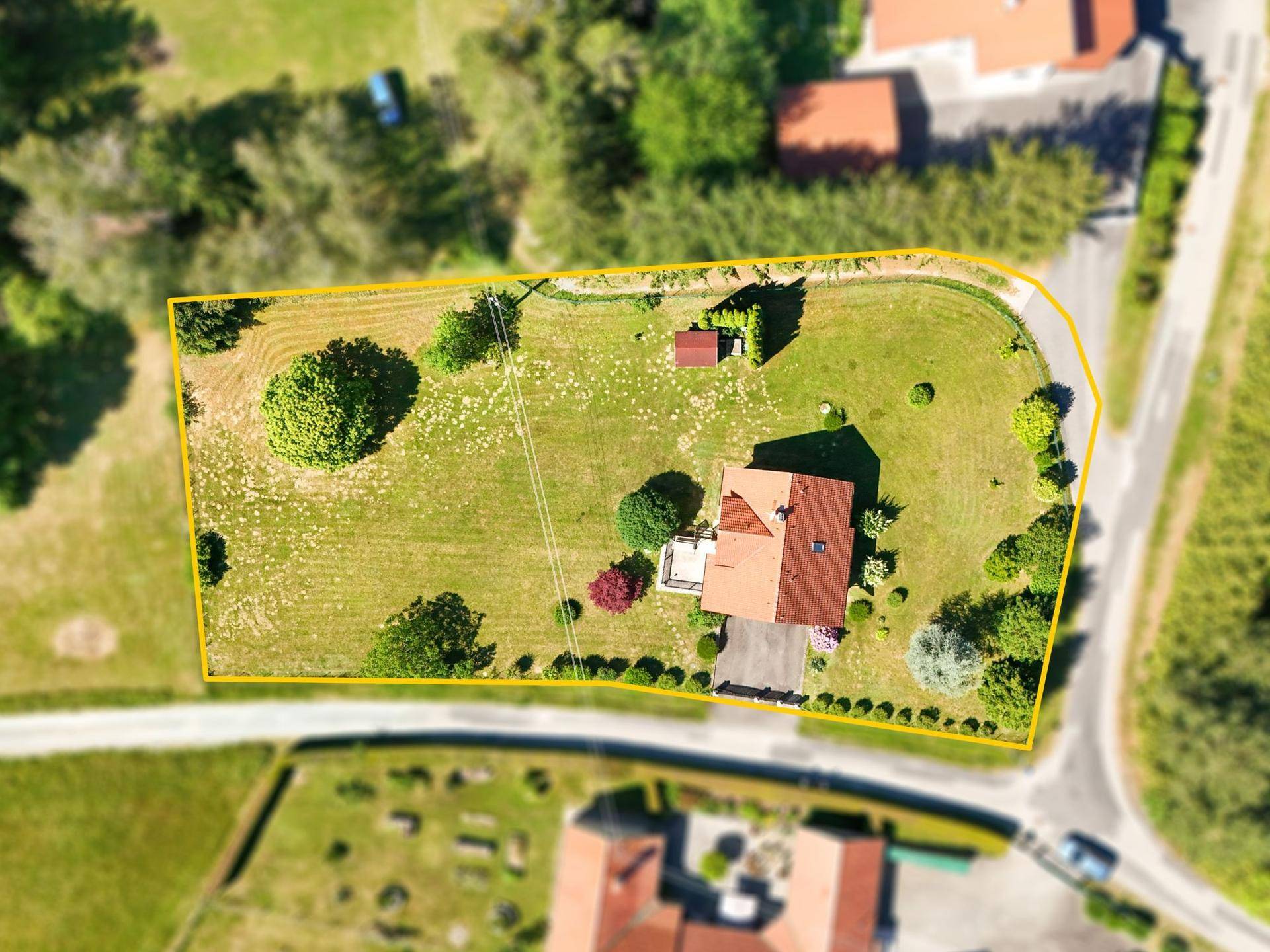Luftaufnahme des Grundstücks mit Einfamilienhaus, großem Garten und angrenzender Straße, umrandet von Bäumen.