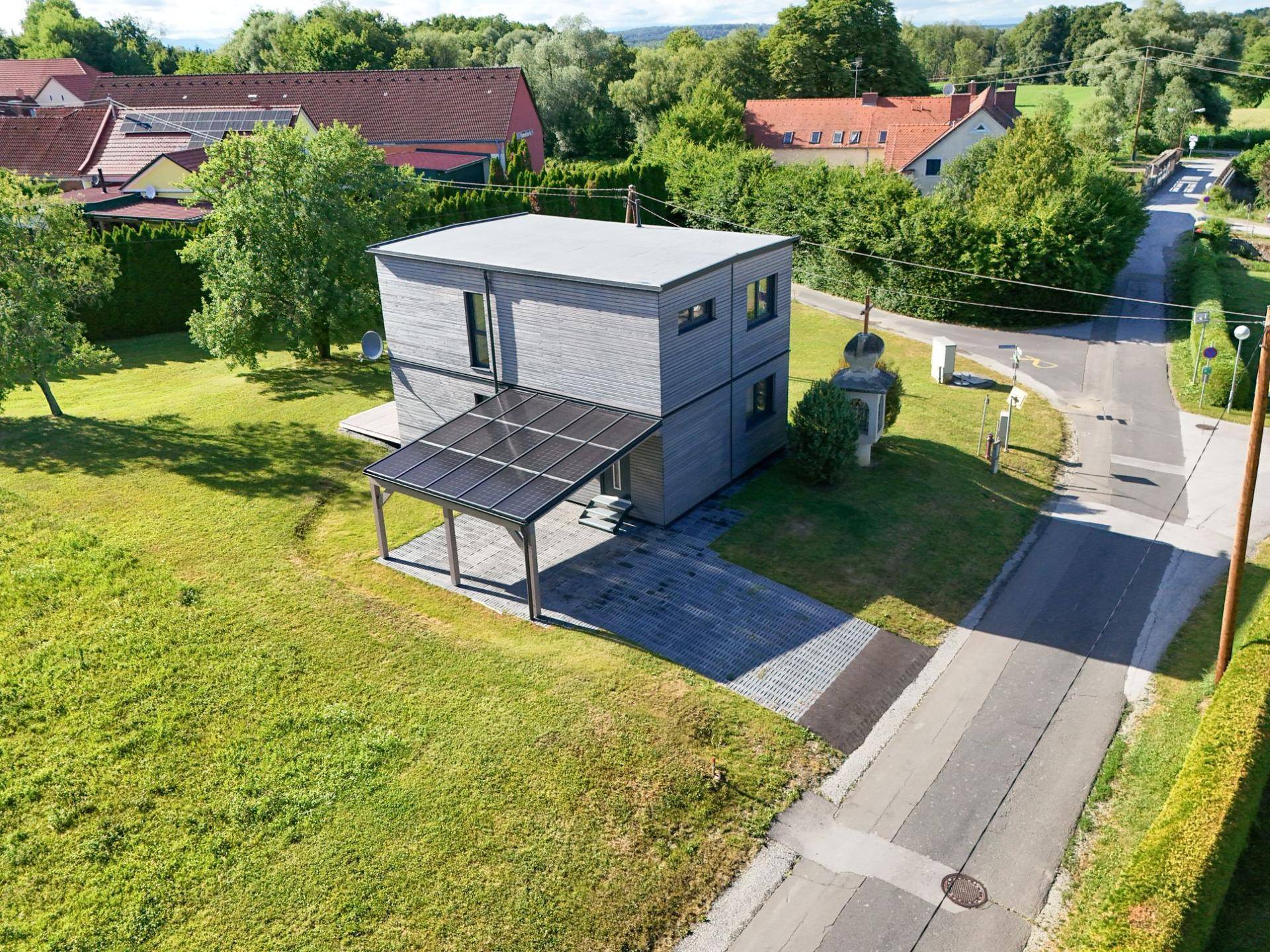 Luftaufnahme des modernen Hauses mit Photovoltaik-Carport und angrenzender ländlicher Siedlung.