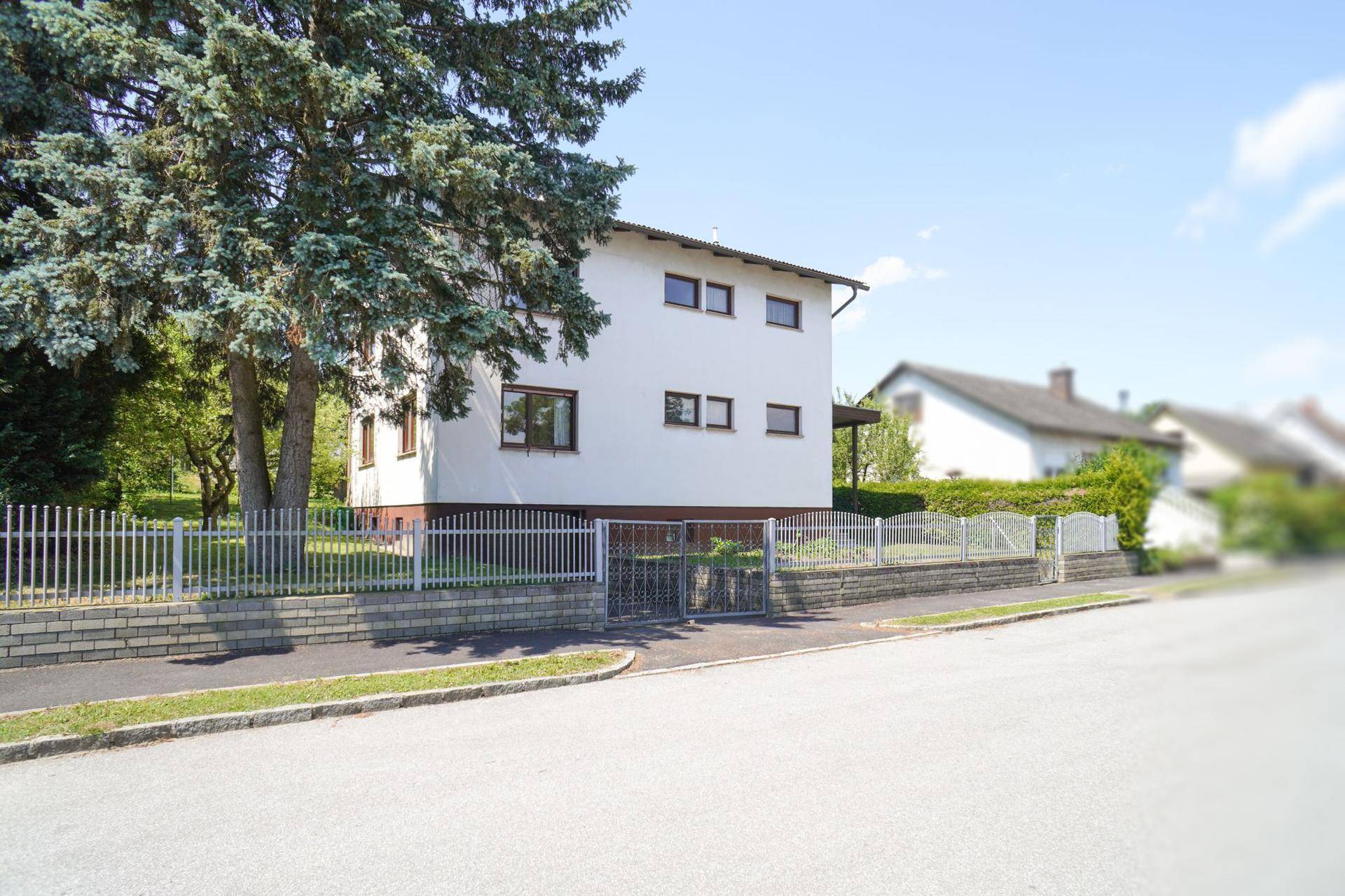 Vorderansicht des Einfamilienhauses von der Straße aus, umzäunt mit einem Vorgarten und altem Baum.