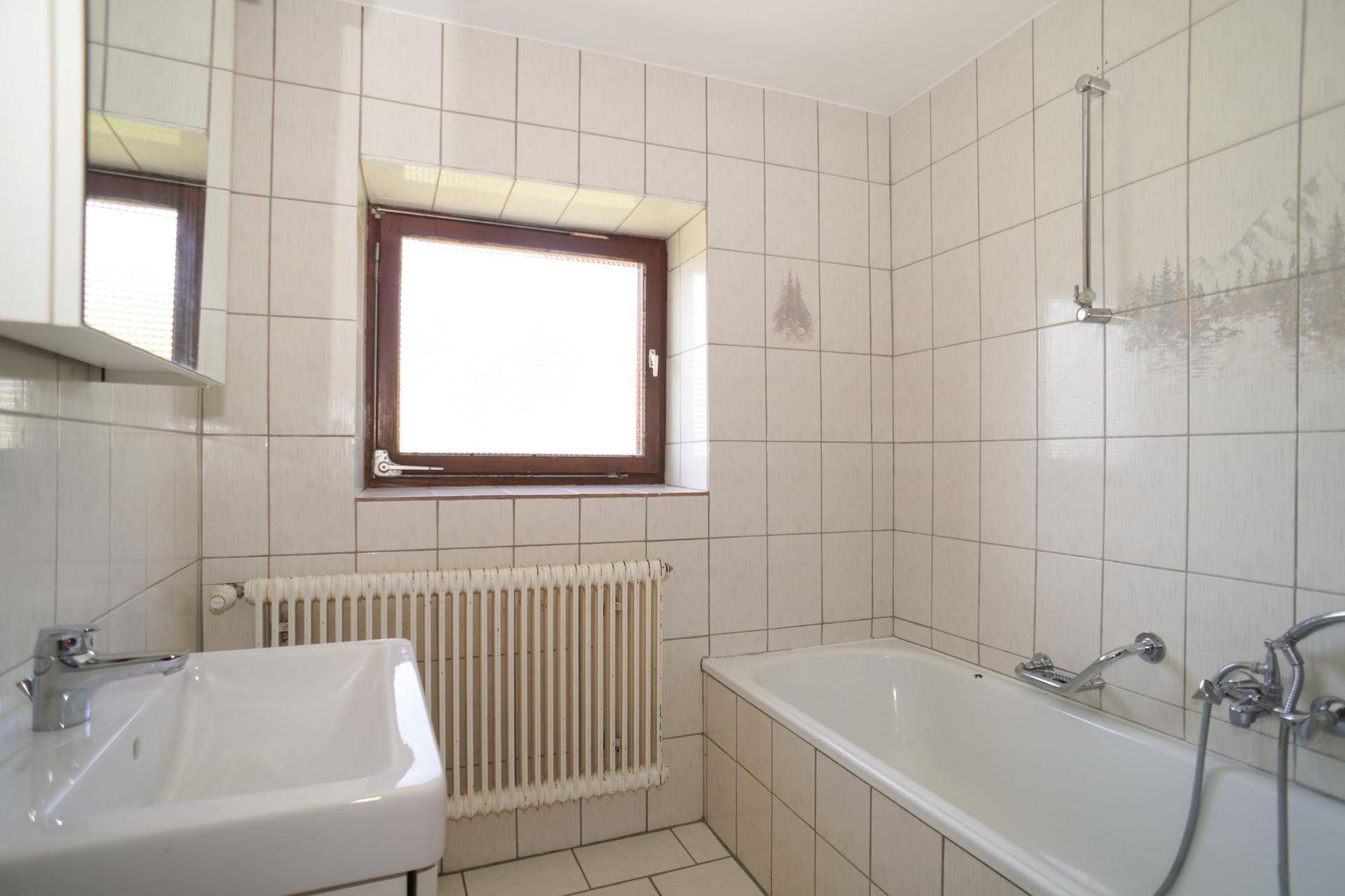 Badezimmer mit weißen Fliesen, Badewanne, Waschbecken und Fenster für Tageslicht.