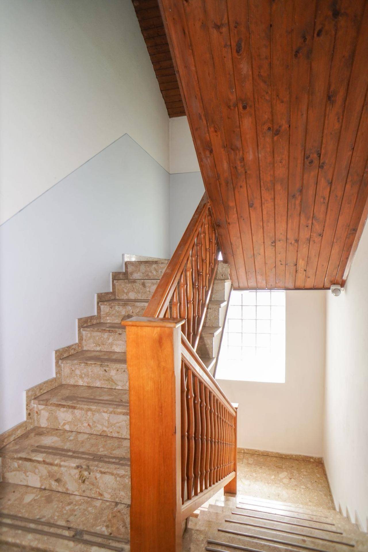 Treppenhaus mit Marmorstufen, Holzgeländer und Holzvertäfelung an der Decke.