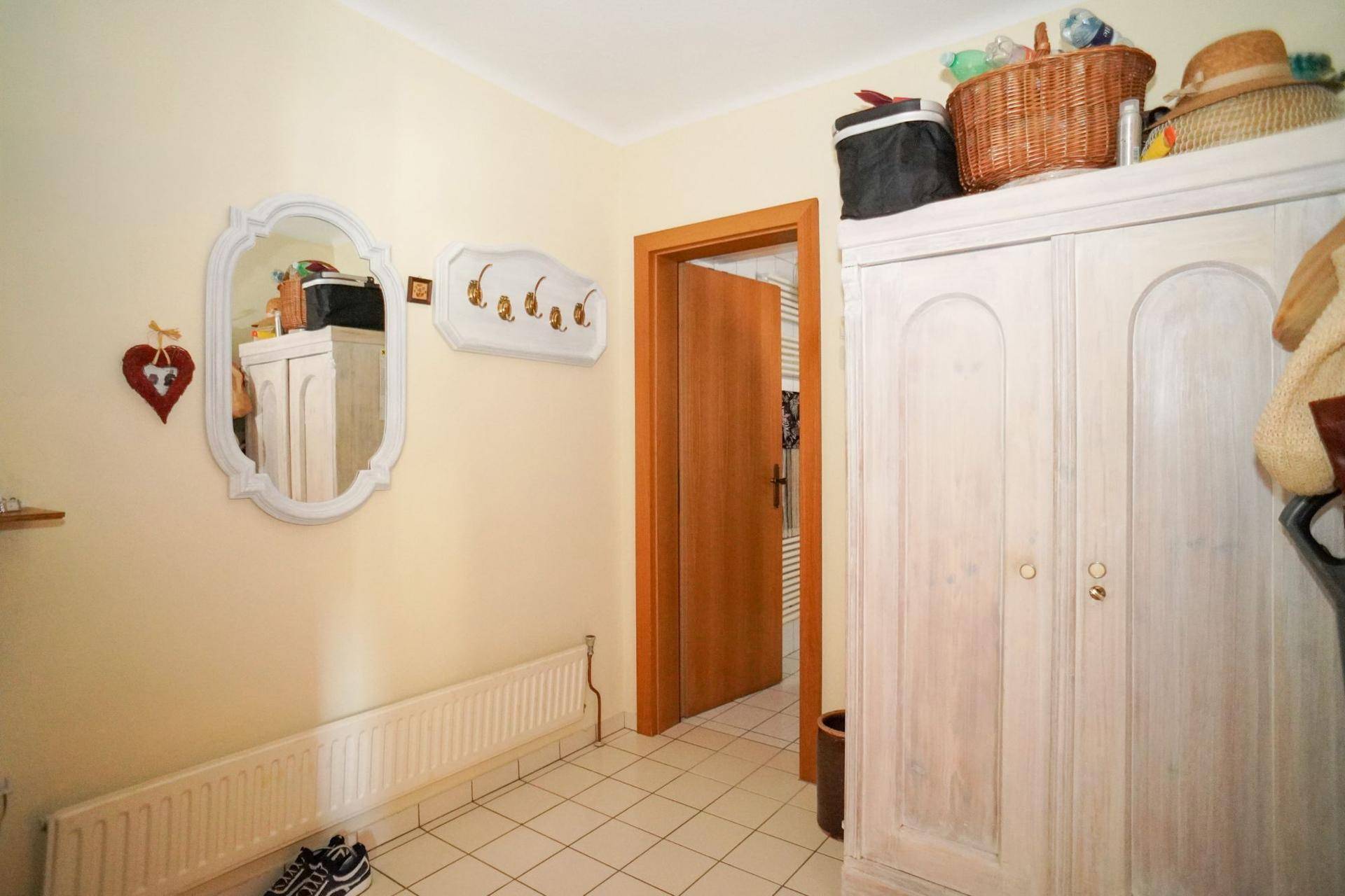 Heller Flur mit weißen Fliesen, Heizkörper und einem großen, weiß gestrichenen Kleiderschrank.