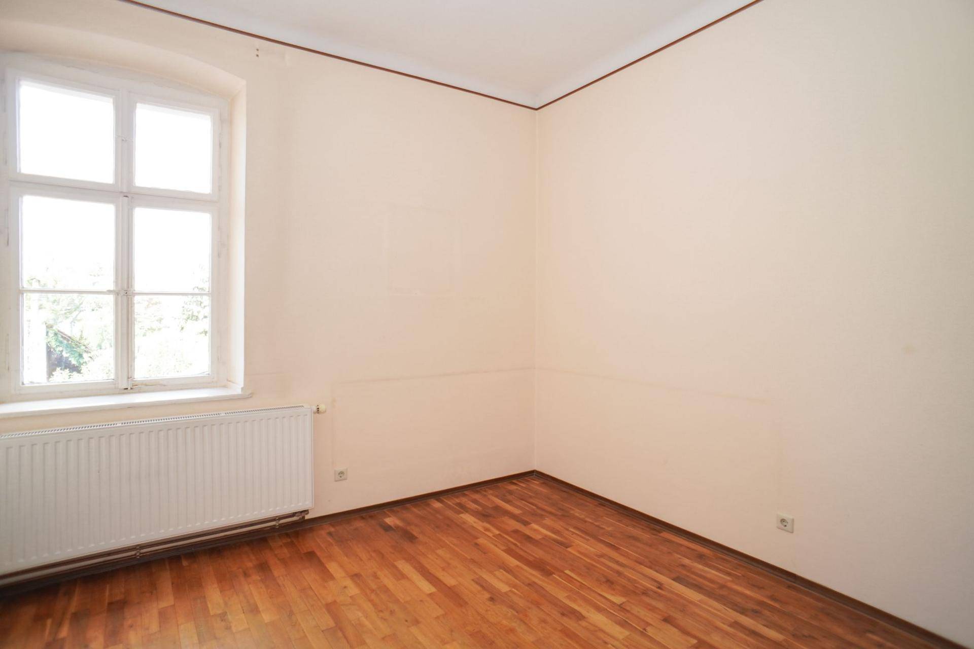 Schlichtes, helles Zimmer mit Holzboden und einem Fenster, ideal als Schlaf- oder Arbeitszimmer.