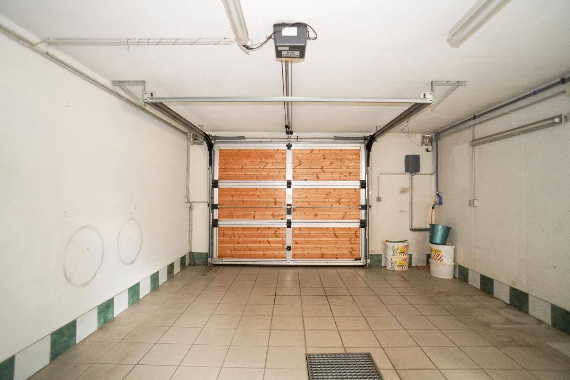Geräumige Garage mit gefliestem Boden, Holzgaragentor und Deckenbeleuchtung.
