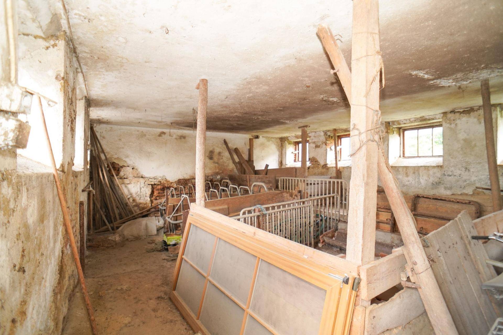 Alter Stallbereich mit Holzbalken, Tierboxen und verschiedenen Baumaterialien, renovierungsbedürftig.