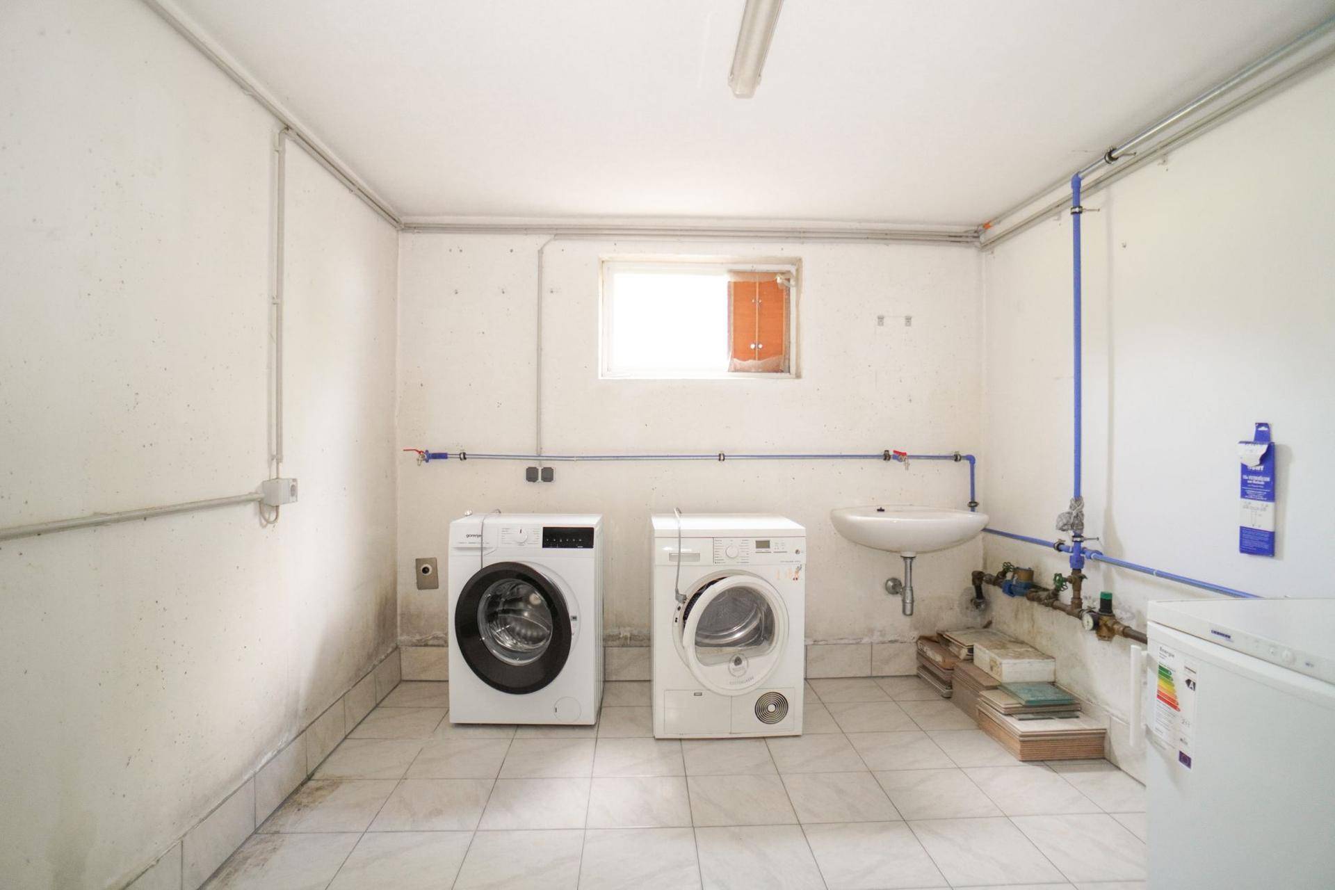 Praktischer Hauswirtschaftsraum mit Waschmaschine, Trockner, Waschbecken und kleinem Fenster.