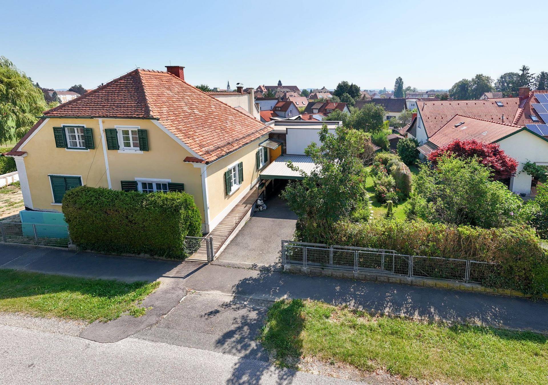 Gesamtansicht des Anwesens von oben mit gelbem Haus, Carport und großem, grünen Garten.
