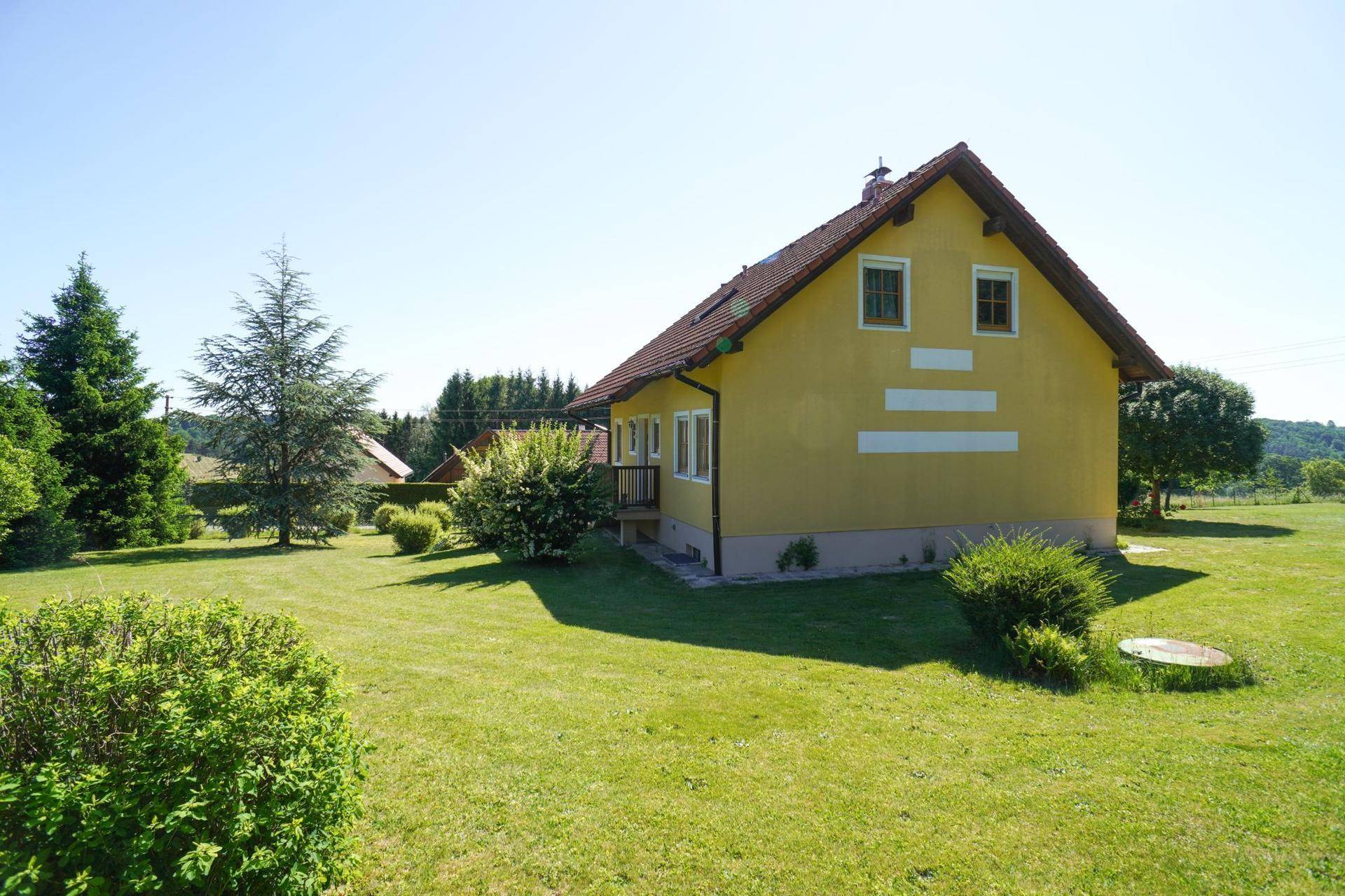 Seitenansicht des gelben Hauses mit gepflegtem Rasen und Sträuchern unter blauem Himmel.