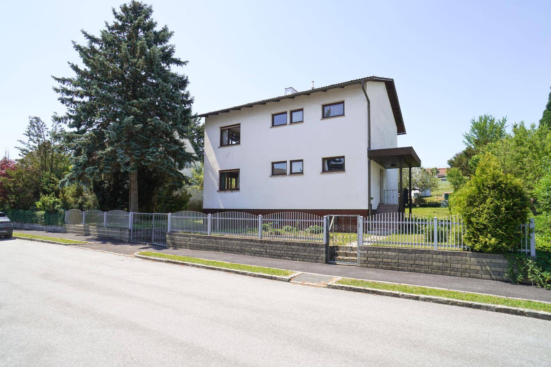 Freistehendes Einfamilienhaus mit weißer Fassade, braunen Fenstern und überdachtem Eingangsbereich.