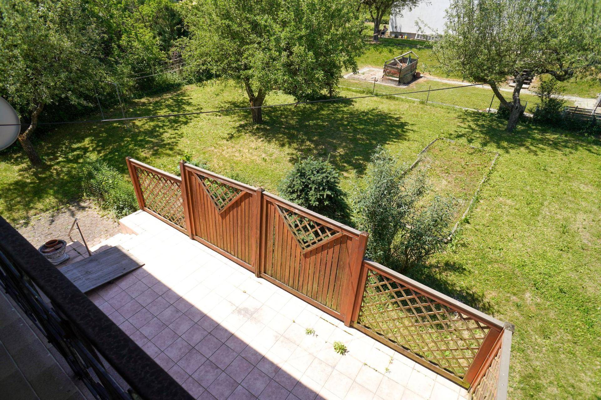 Blick vom Balkon auf den weitläufigen grünen Garten mit altem Baumbestand und viel Platz im Freien.