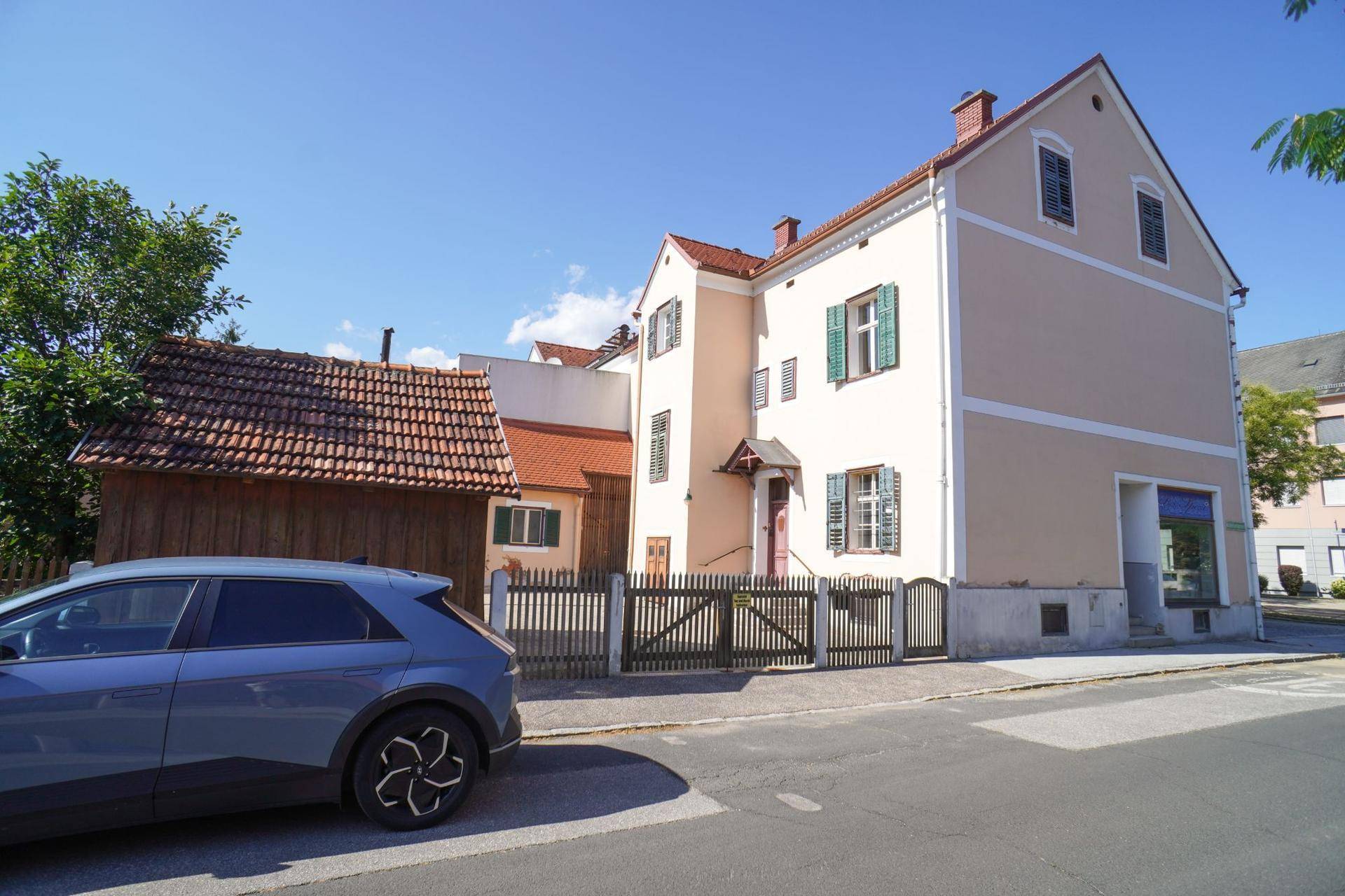 Traditionelles Gebäude mit heller Fassade und grünen Fensterläden an einer ruhigen Straße.