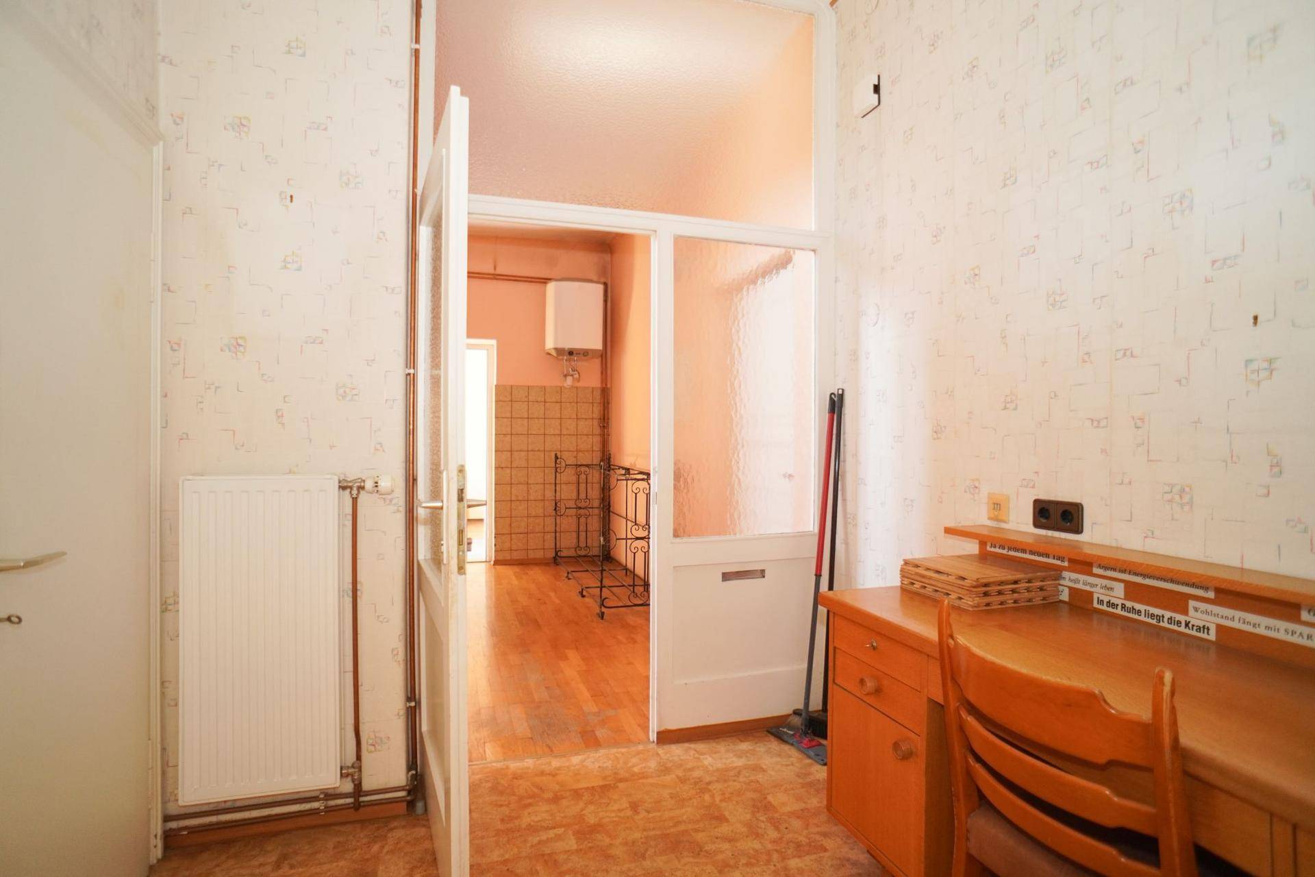 Eingangsbereich mit Tapete und Durchgang zu einem weiteren Raum, mit Schreibtisch.