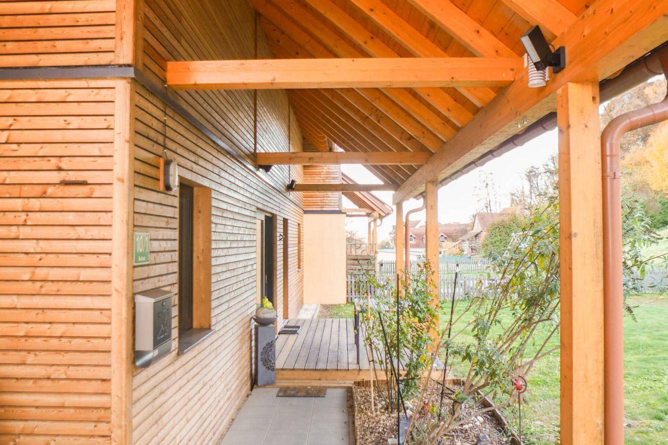 Überdachter Eingangsbereich mit Holzverkleidung, Holzbalken und Blick auf den Garten.