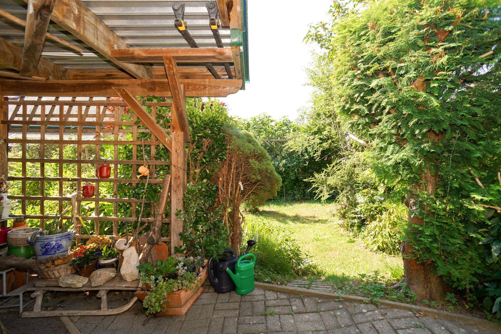 Gemütlicher Terrassenbereich unter einer Holzpergola mit Pflanzen und Blick auf den Garten.