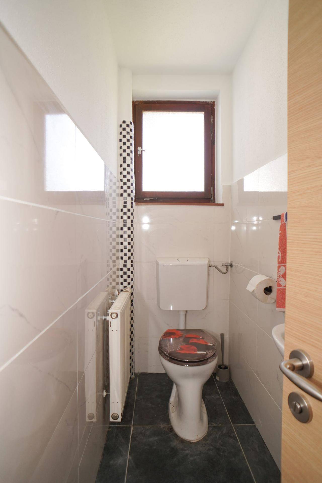Separates WC mit Fenster, Fliesenboden und modernem Mosaik-Detail.