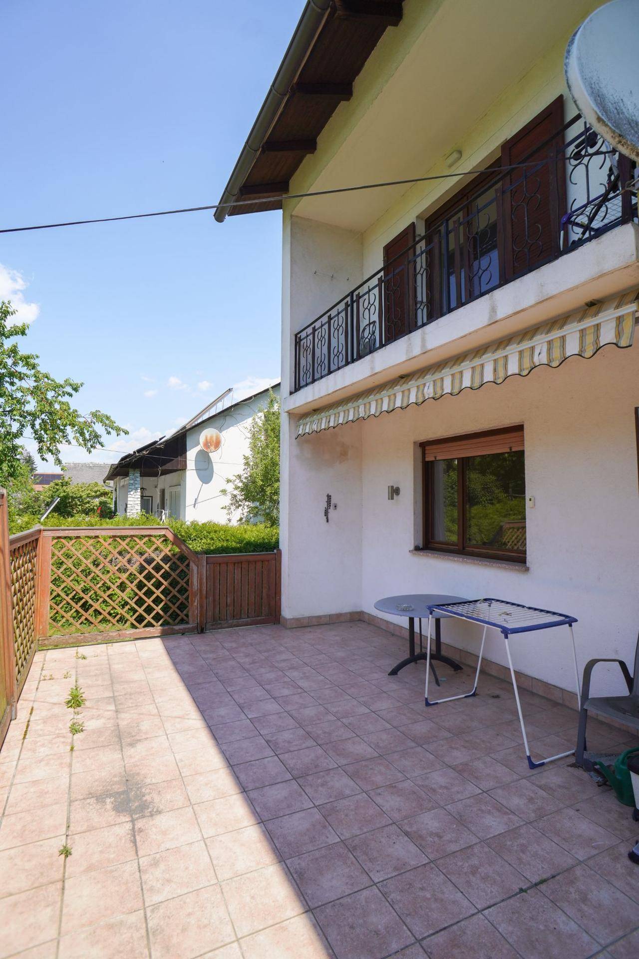Geflieste Terrasse mit Markise und Blick auf den Garten, ideal für Mahlzeiten im Freien.