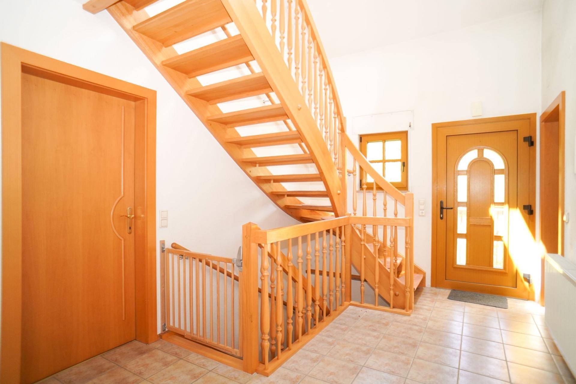 Heller Eingangsbereich mit Holztreppe, gefliestem Boden und Holztüren, die zu weiteren Räumen führen.