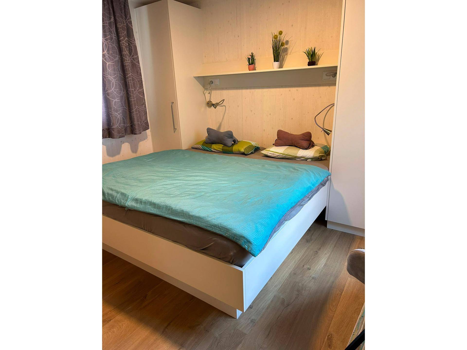 Schlafzimmer mit Doppelbett, türkiser Bettwäsche und integrierten Schränken.