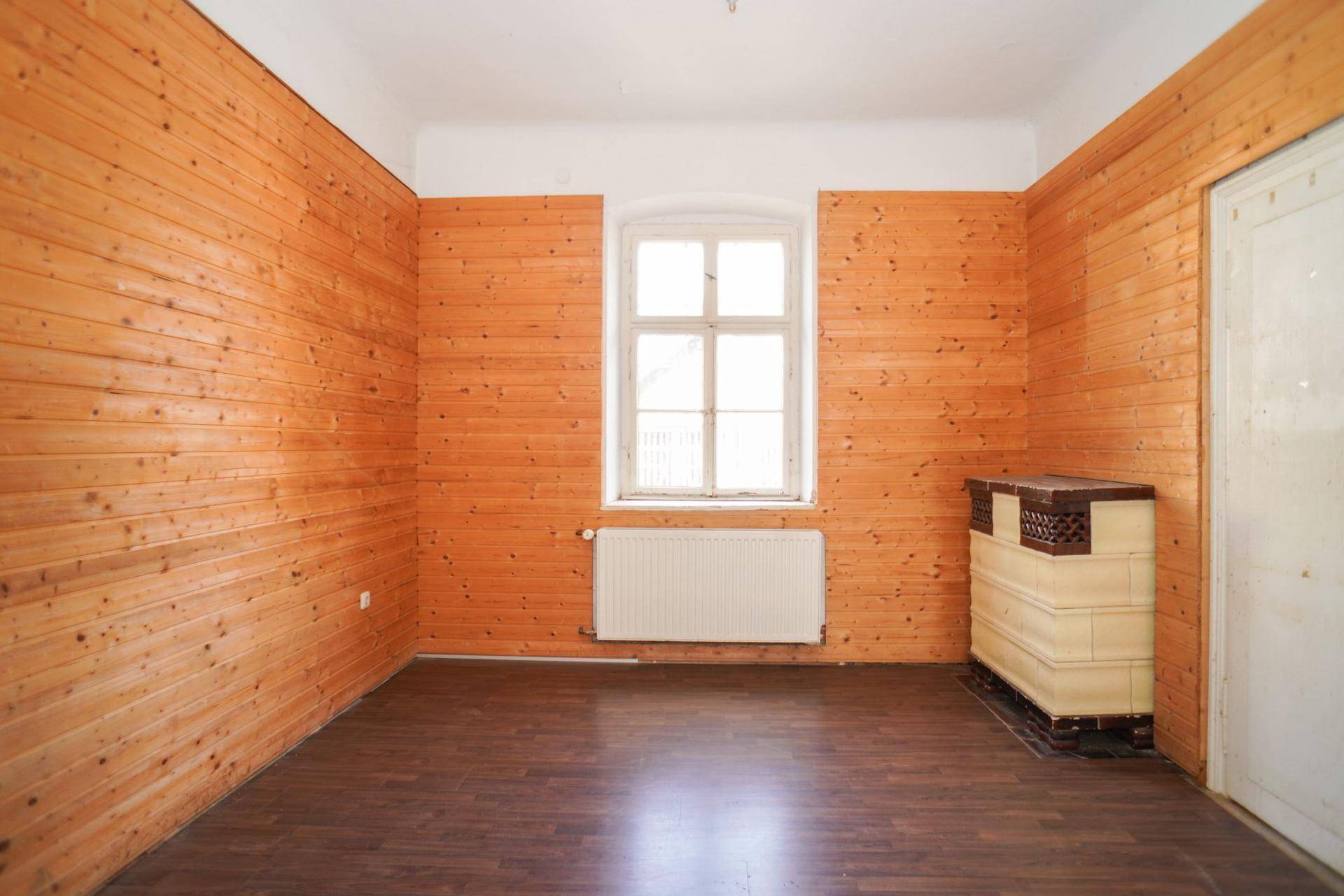 Rustikaler Raum mit Holzvertäfelung, einem traditionellen Kachelofen und einem Fenster.