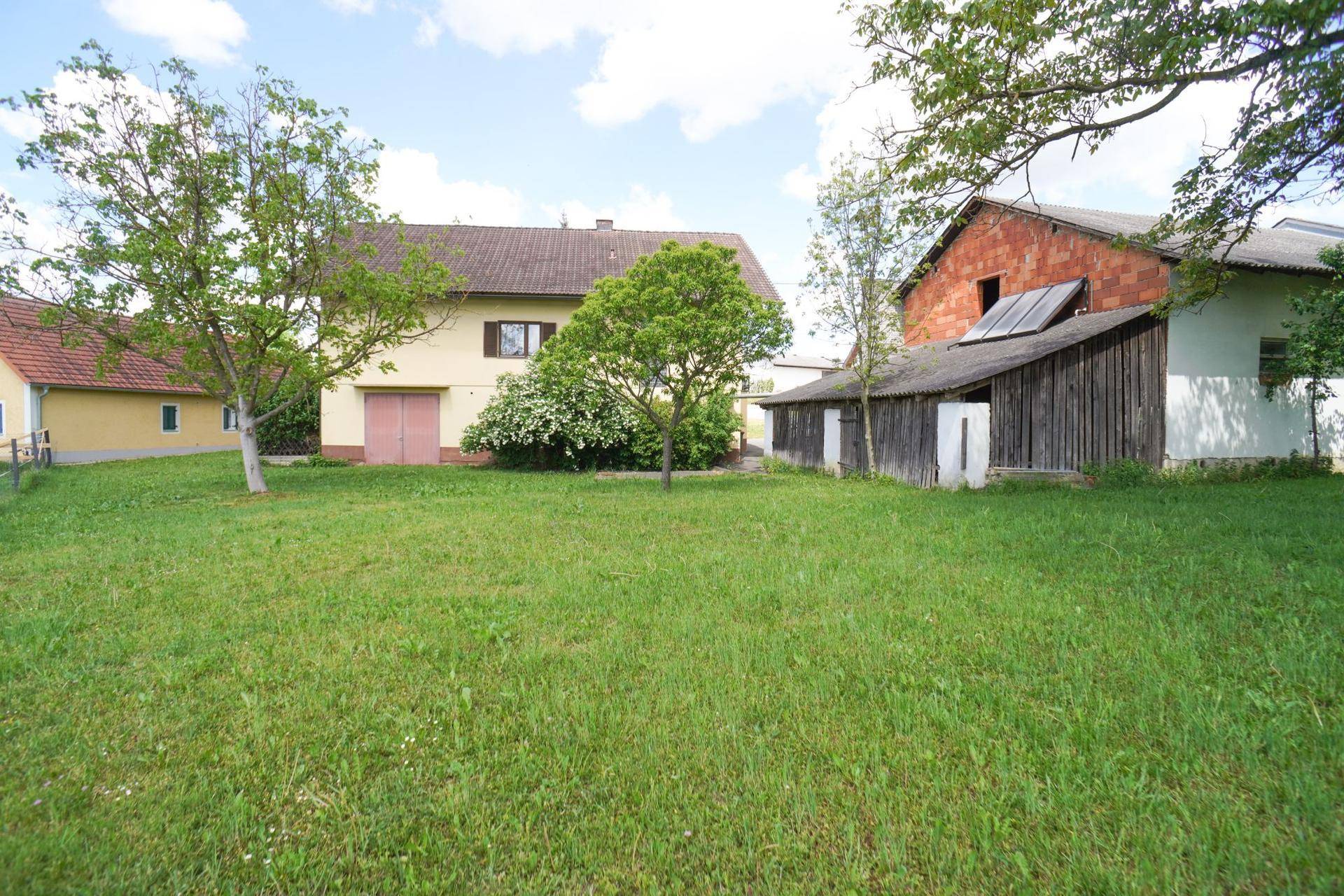 Weitläufiger Gartenbereich mit Rasenfläche, Bäumen und Blick auf das Wohnhaus und Nebengebäude.