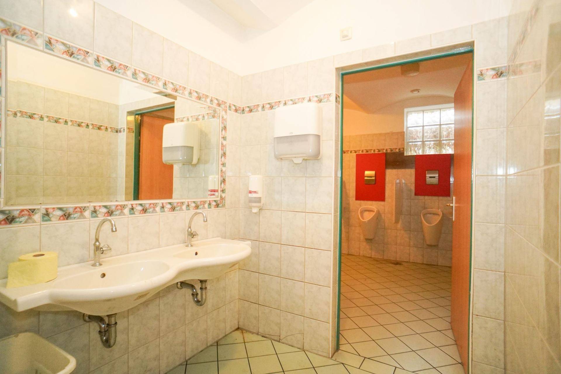 Öffentliche Toilettenanlage mit Doppelwaschbecken, Urinalen und gefliesten Wänden.