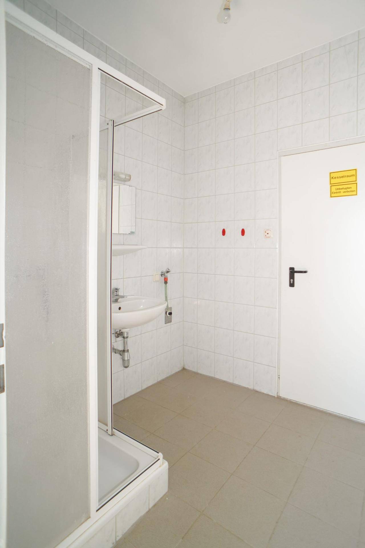 Einfaches Badezimmer mit Duschkabine, Waschbecken und hellen Fliesen an Wänden und Boden.