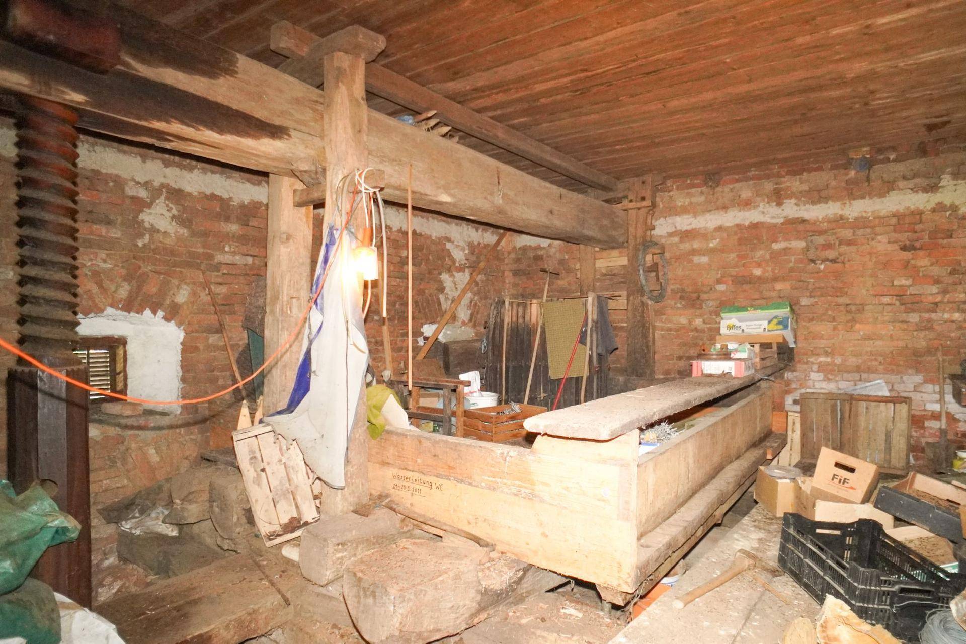 Rustikaler Raum mit freiliegenden Ziegelwänden und Holzbalken, genutzt als Lagerbereich.