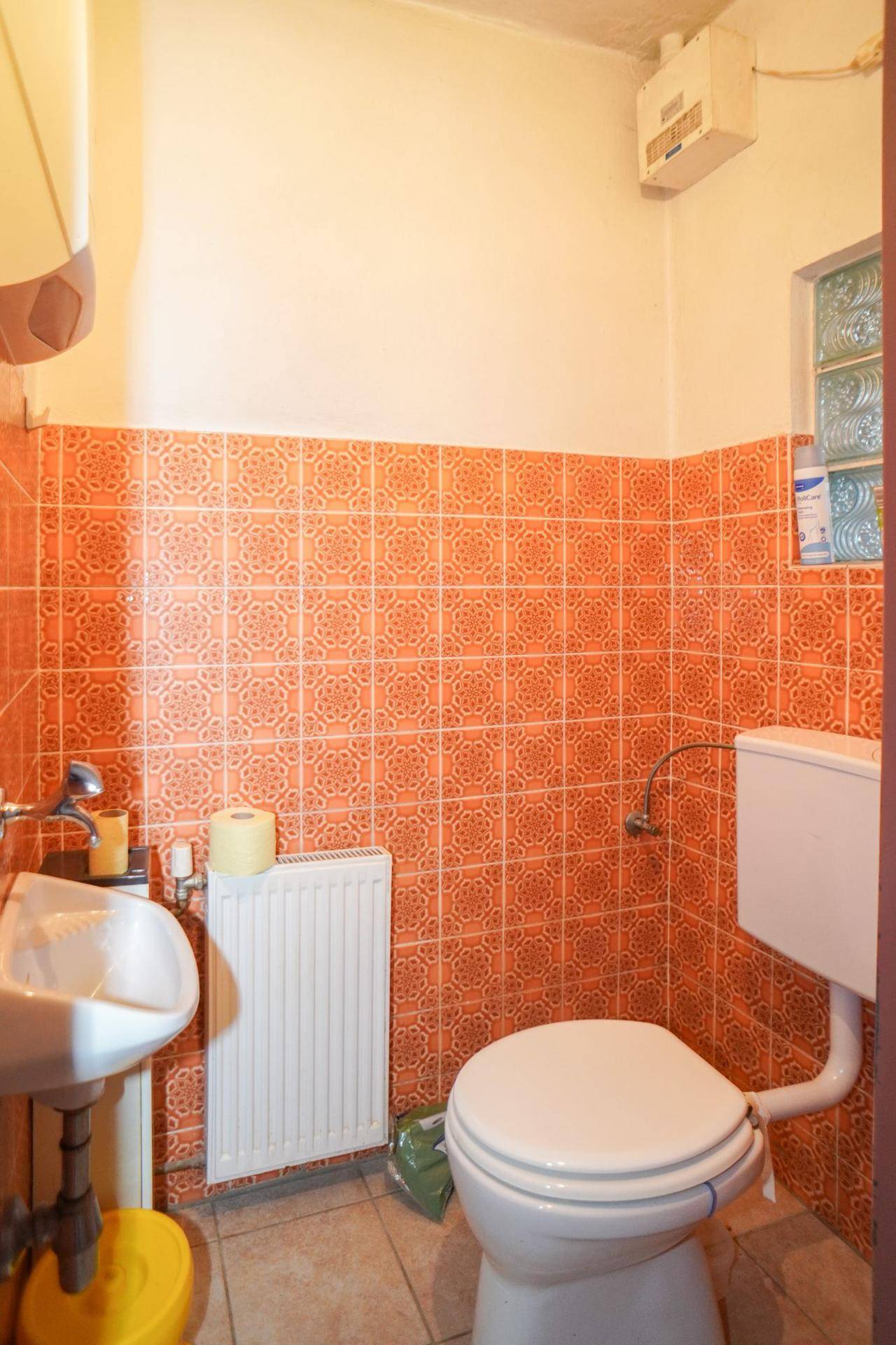 Separate Toilette mit orangefarbenen Fliesen, Waschbecken und Heizkörper.