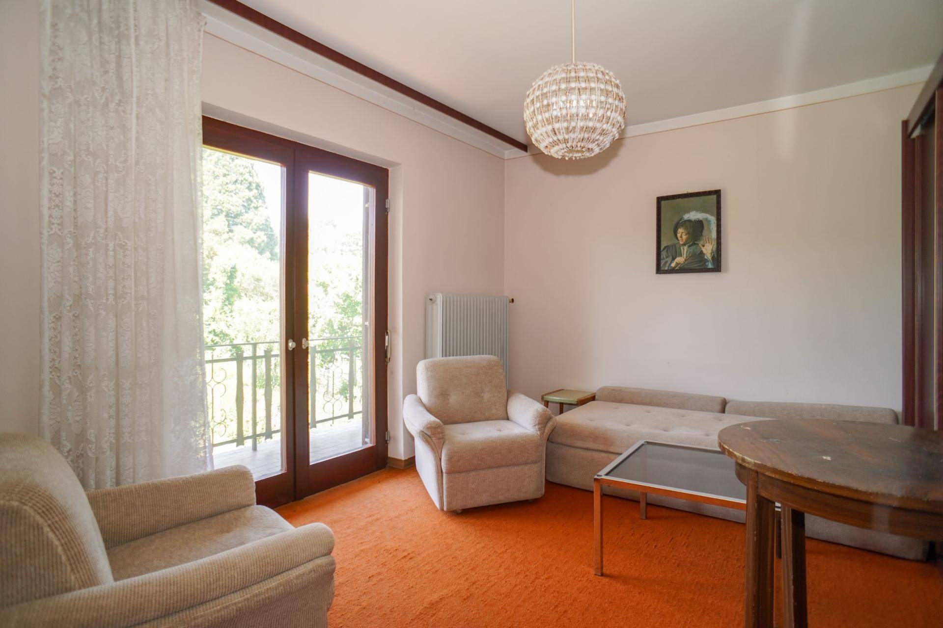 Wohnzimmer mit beigem Sofa, Teppichboden und Balkonzugang mit Blick ins Grüne.