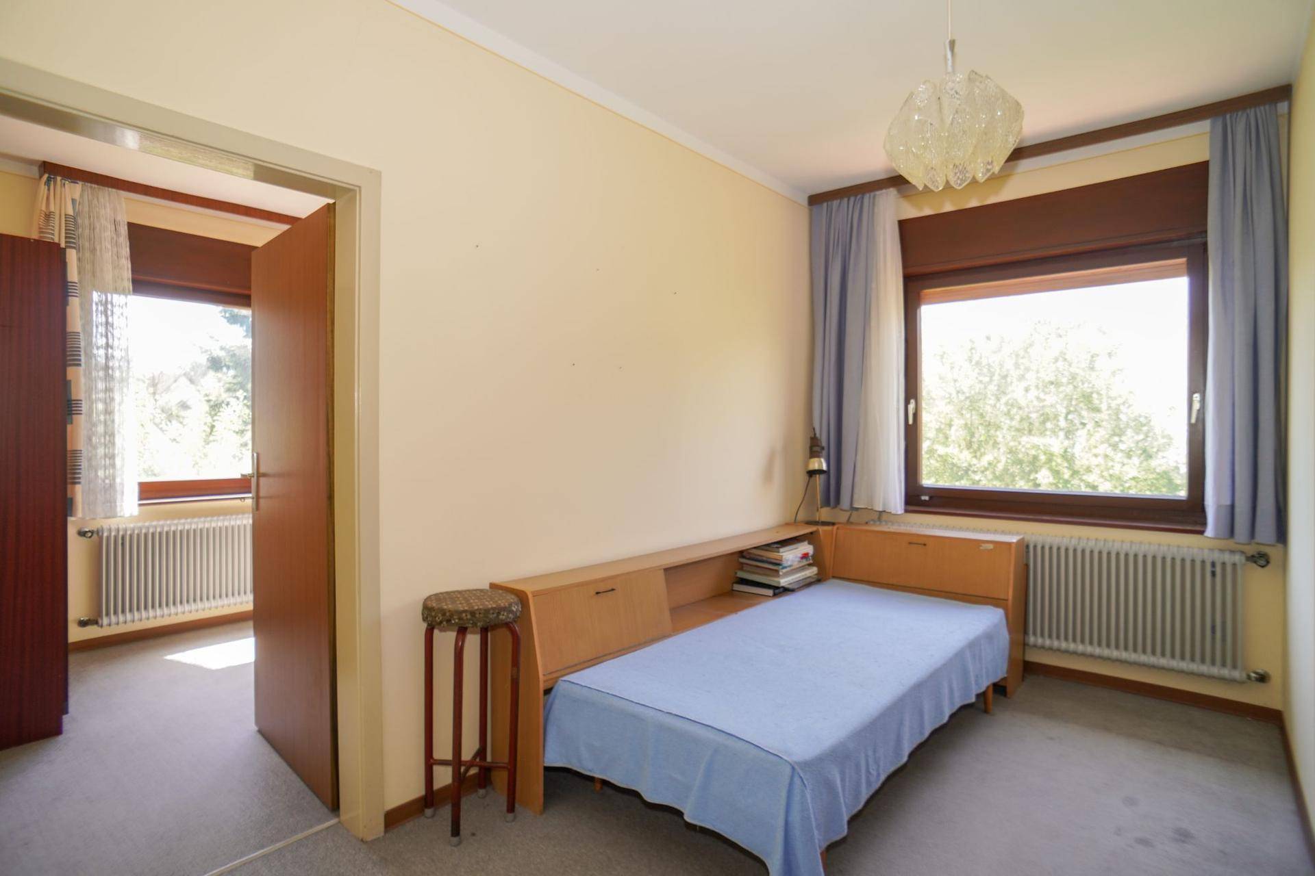 Helles Schlafzimmer mit Einzelbett, Teppichboden und großem Fenster mit Ausblick.