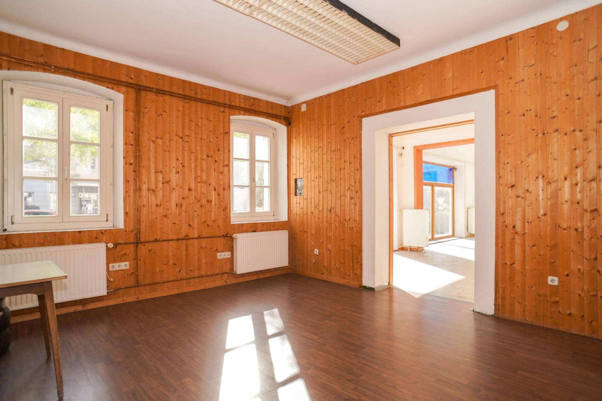 Gemütlicher Raum mit Holzvertäfelung an den Wänden und dunklem Laminatboden, hell durch Fenster.