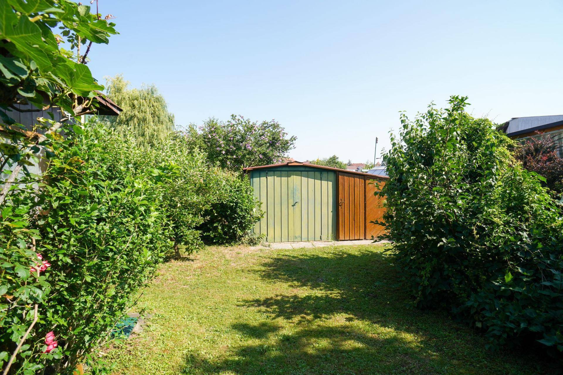 Großer Garten mit Rasenfläche, Sträuchern und einem weiteren Gartenhaus im Hintergrund.