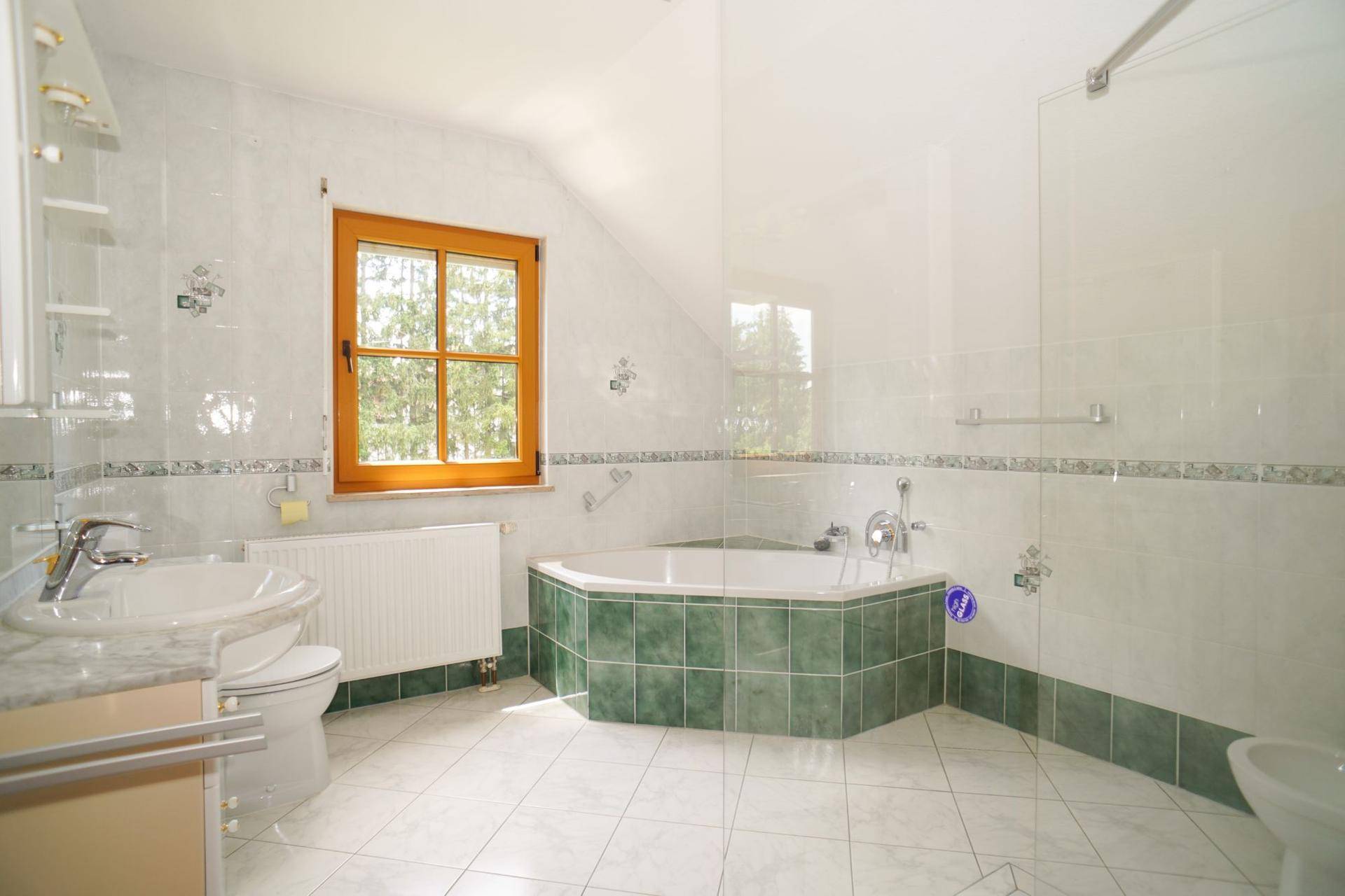 Dachgeschoss-Badezimmer mit Eckbadewanne, Waschbecken und WC, hell gefliest mit grünen Akzenten.