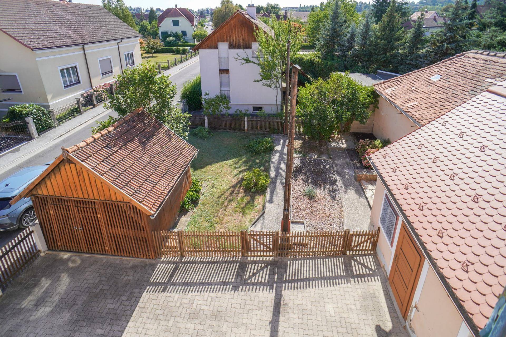 Hinterhof mit Garage, gepflastertem Bereich und einem kleinen Garten, umgeben von einem Zaun.