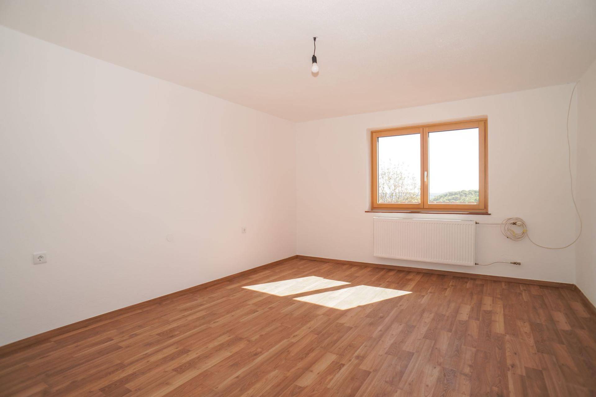 Helles Zimmer mit Holzboden, großem Fenster und Heizkörper, ideal als Schlafzimmer.