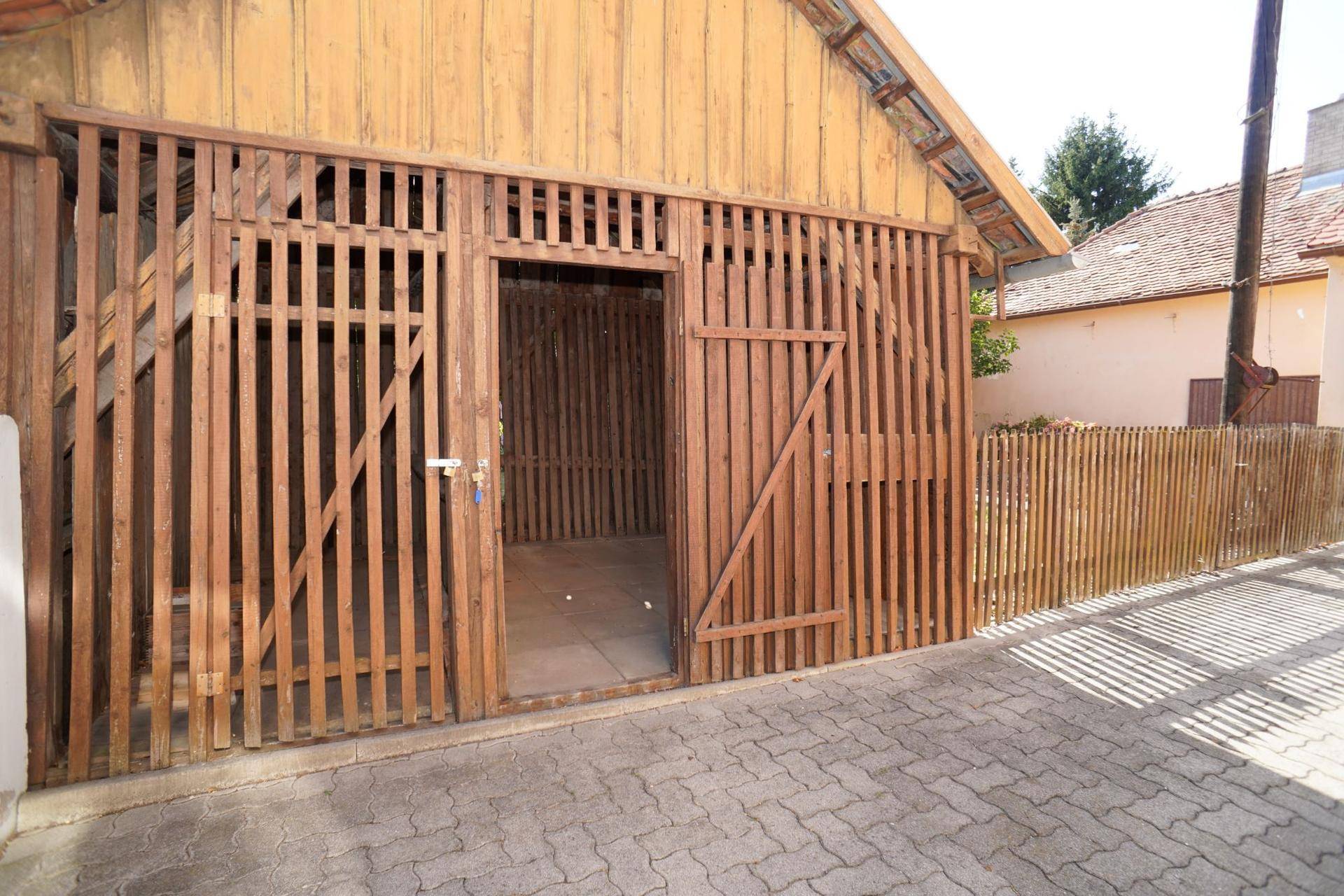 Rustikales Holzgebäude mit Lattenwänden und gepflastertem Vorplatz, ideal als Scheune oder Lager.