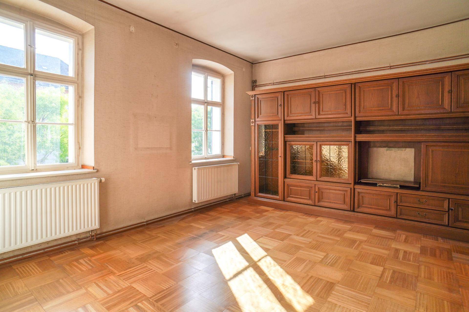 Geräumiges Wohnzimmer mit Fischgrätparkett und einem großen, traditionellen Holzschrank.