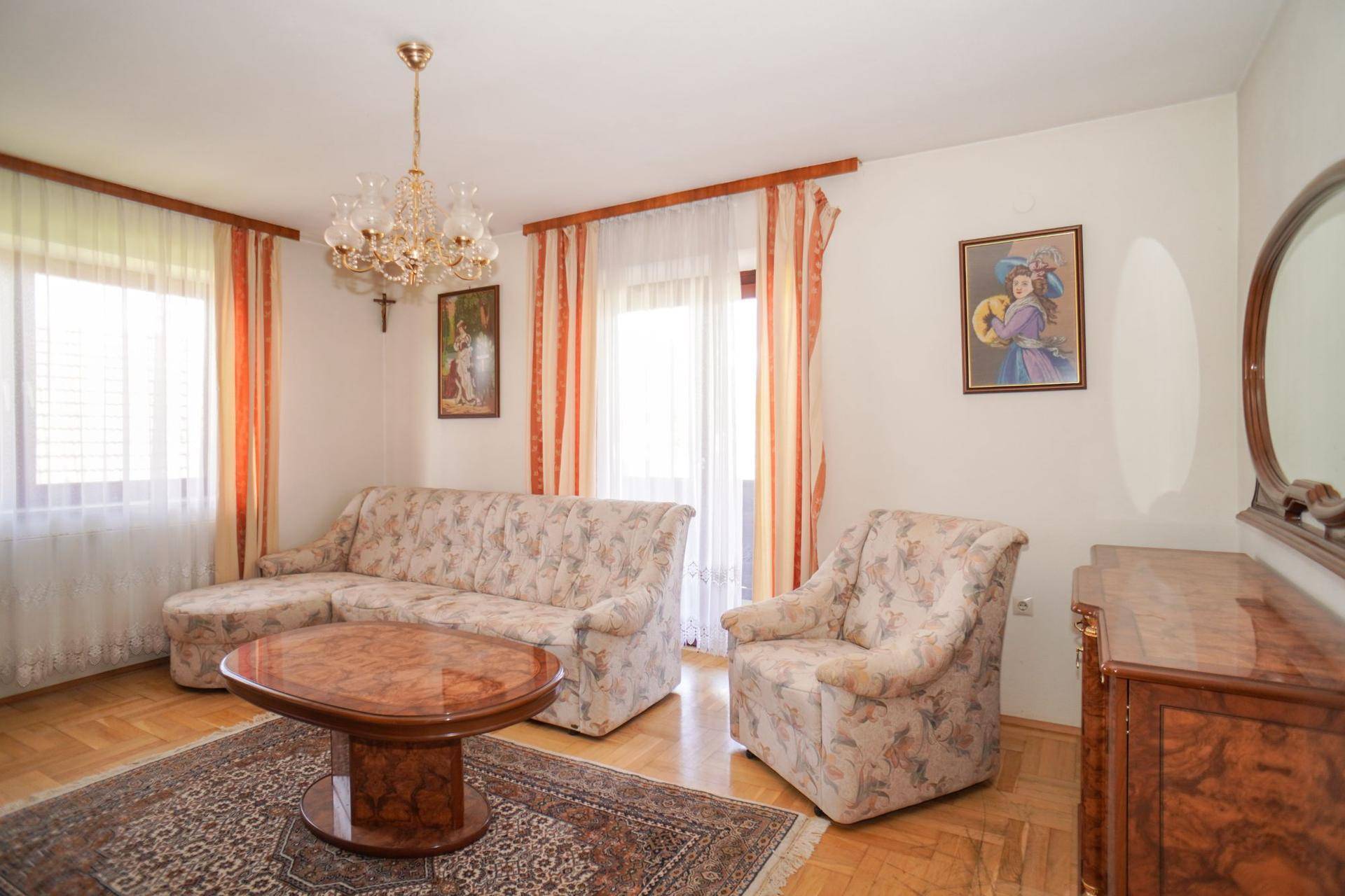 Gemütliches Wohnzimmer mit Parkettboden, floral gemusterten Möbeln und Zugang zum Balkon.