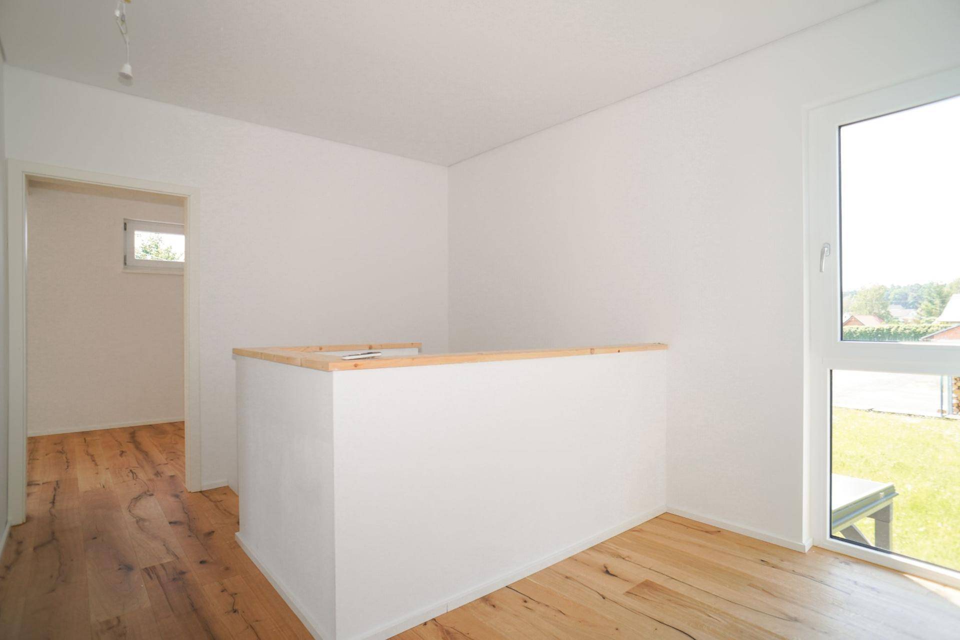Heller Flurbereich mit Holzboden, einer halbhohen Wand und einem Fenster mit Ausblick.