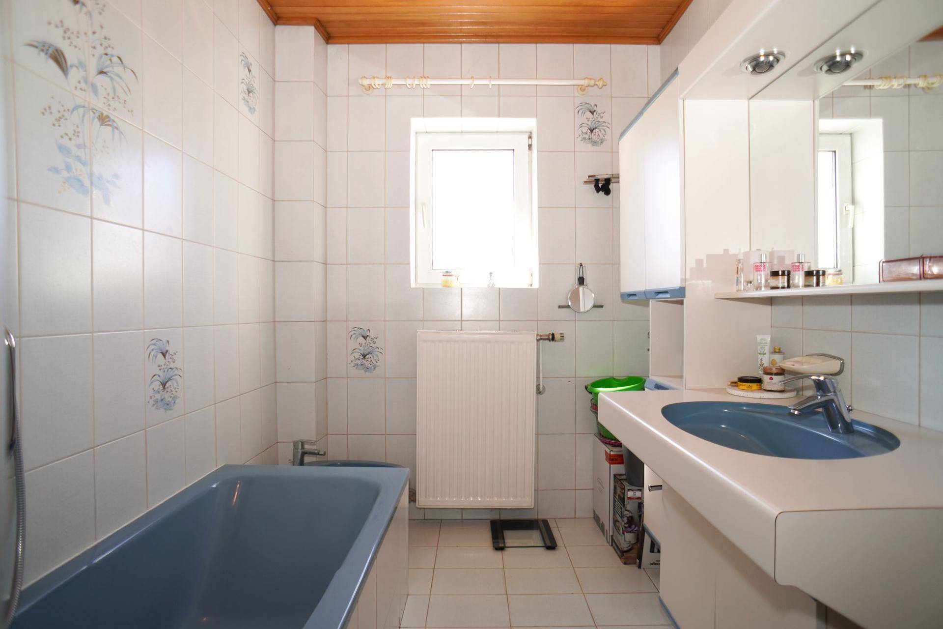 Badezimmer mit blauer Badewanne, passendem Waschbecken, weißen Fliesen und Holzdecke.